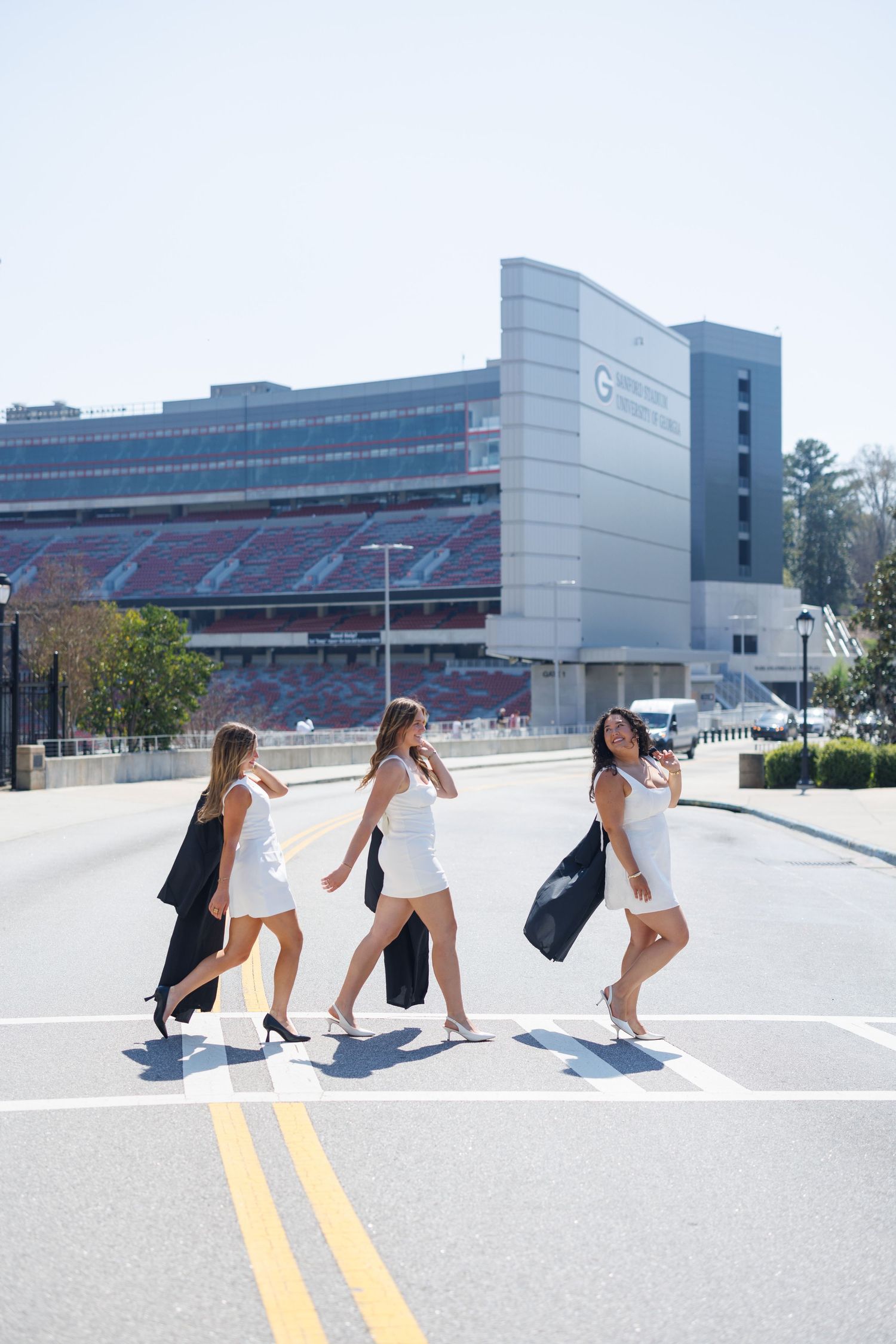 Four friends walking in a sequence across a parking lot with modern office buildings in the background.