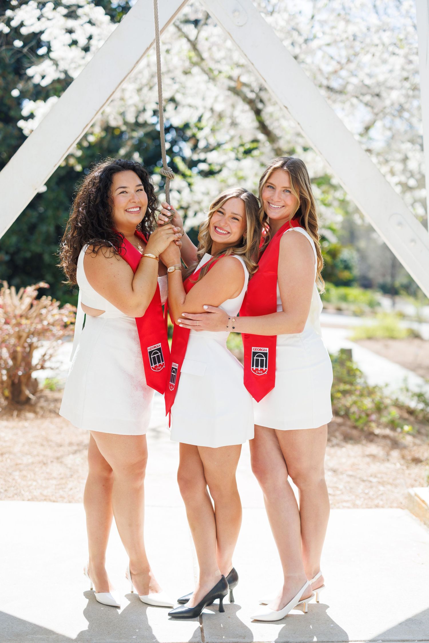 Three friends in red and white outfits pose together outdoors on a sunny day during a photo session.