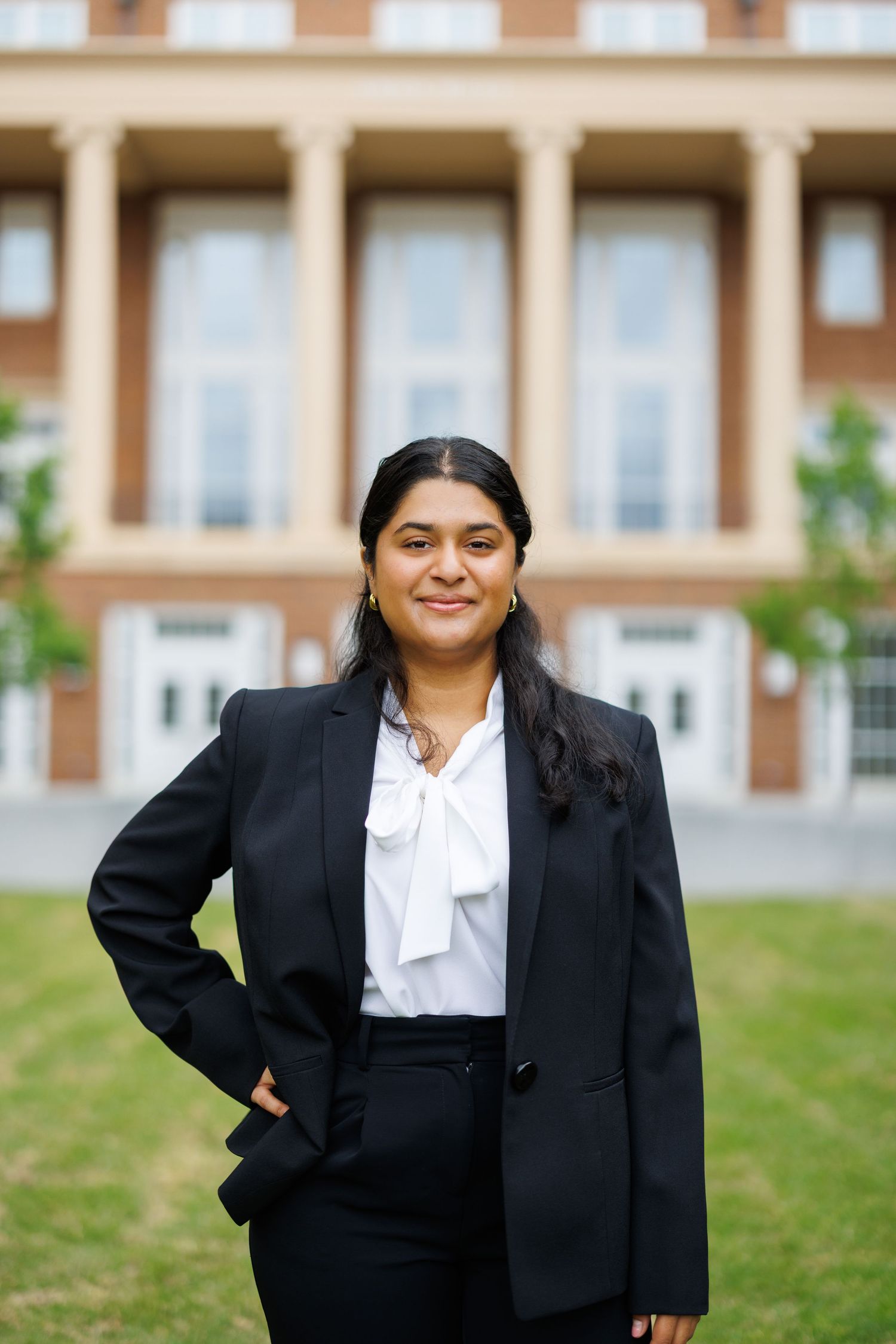 Professional woman in black blazer and white blouse standing outdoors in front of a brick building.