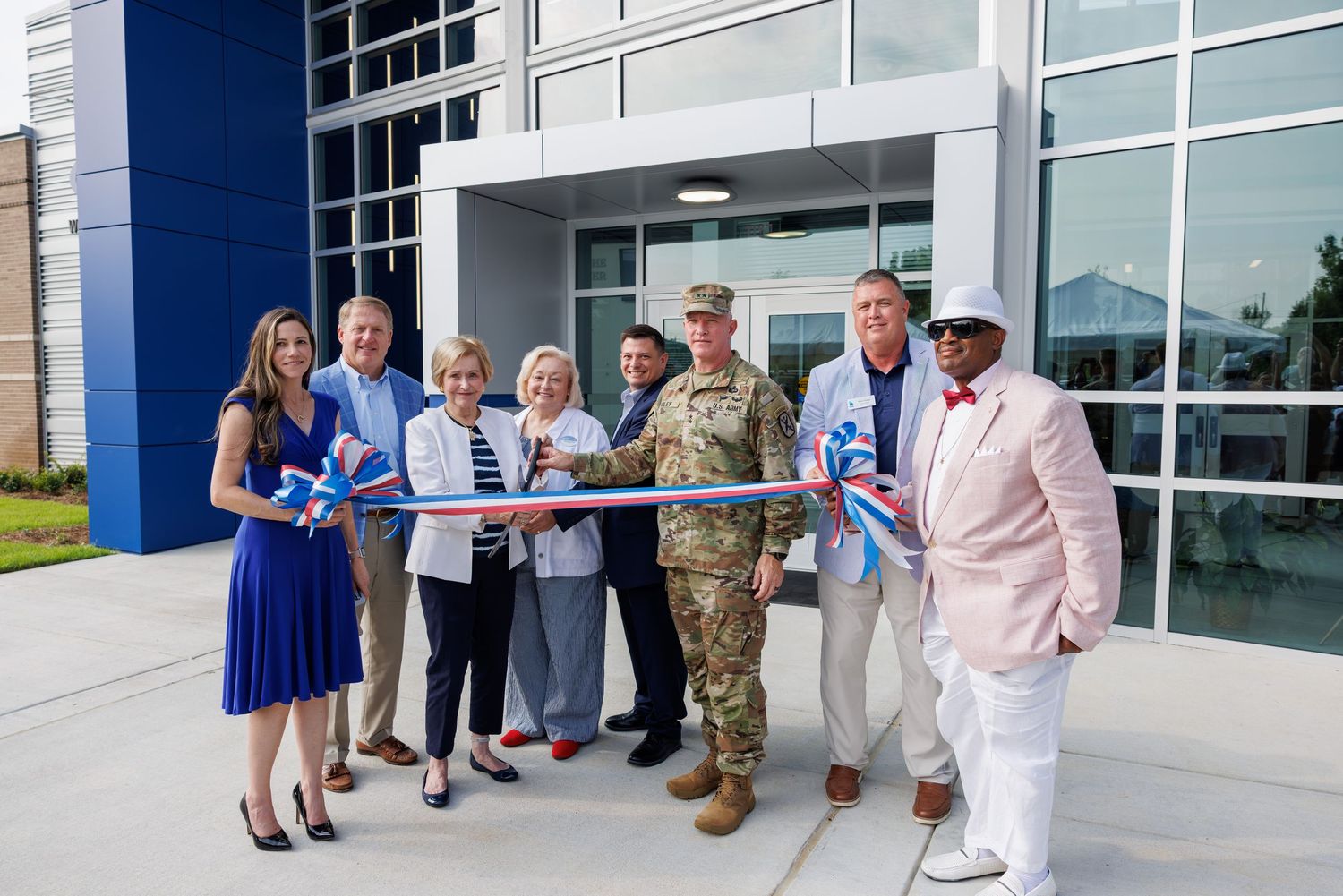 Group of officials cutting a ribbon at a building grand opening ceremony, with one person in military uniform.