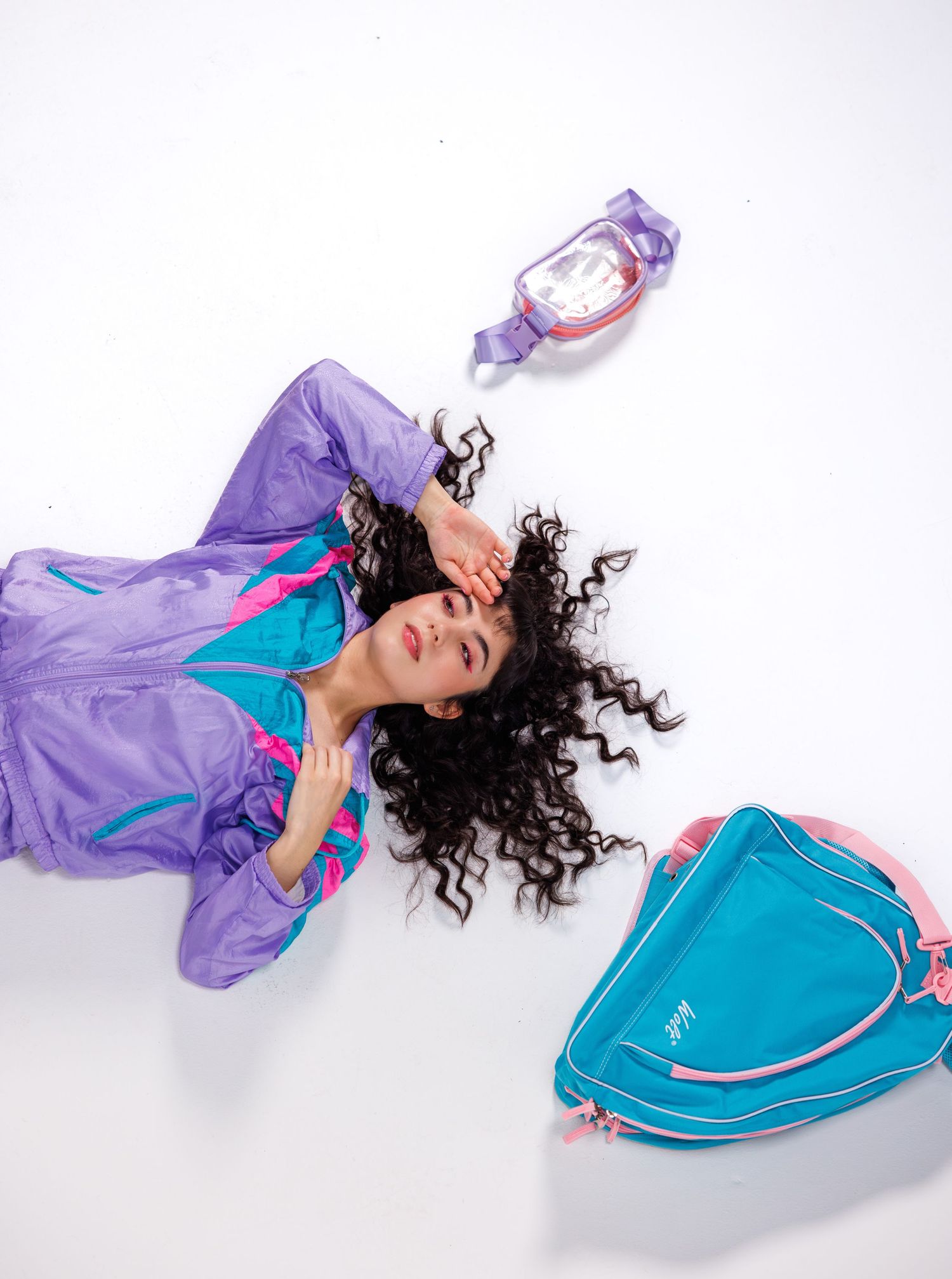 Model in purple and turquoise windbreaker poses dramatically against white background.