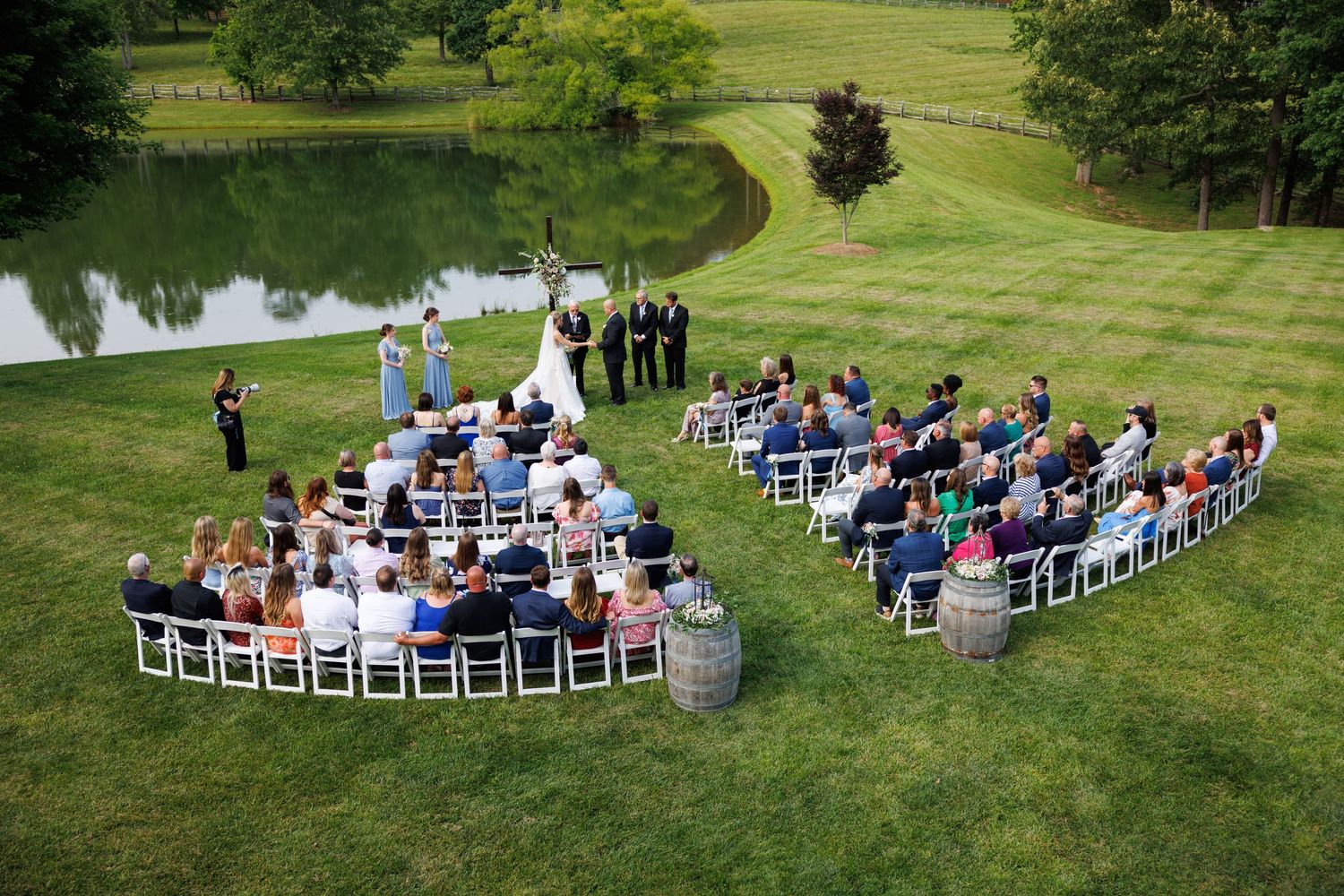 Outdoor wedding ceremony setup with white chairs arranged in rows on a green lawn overlooking a lake.