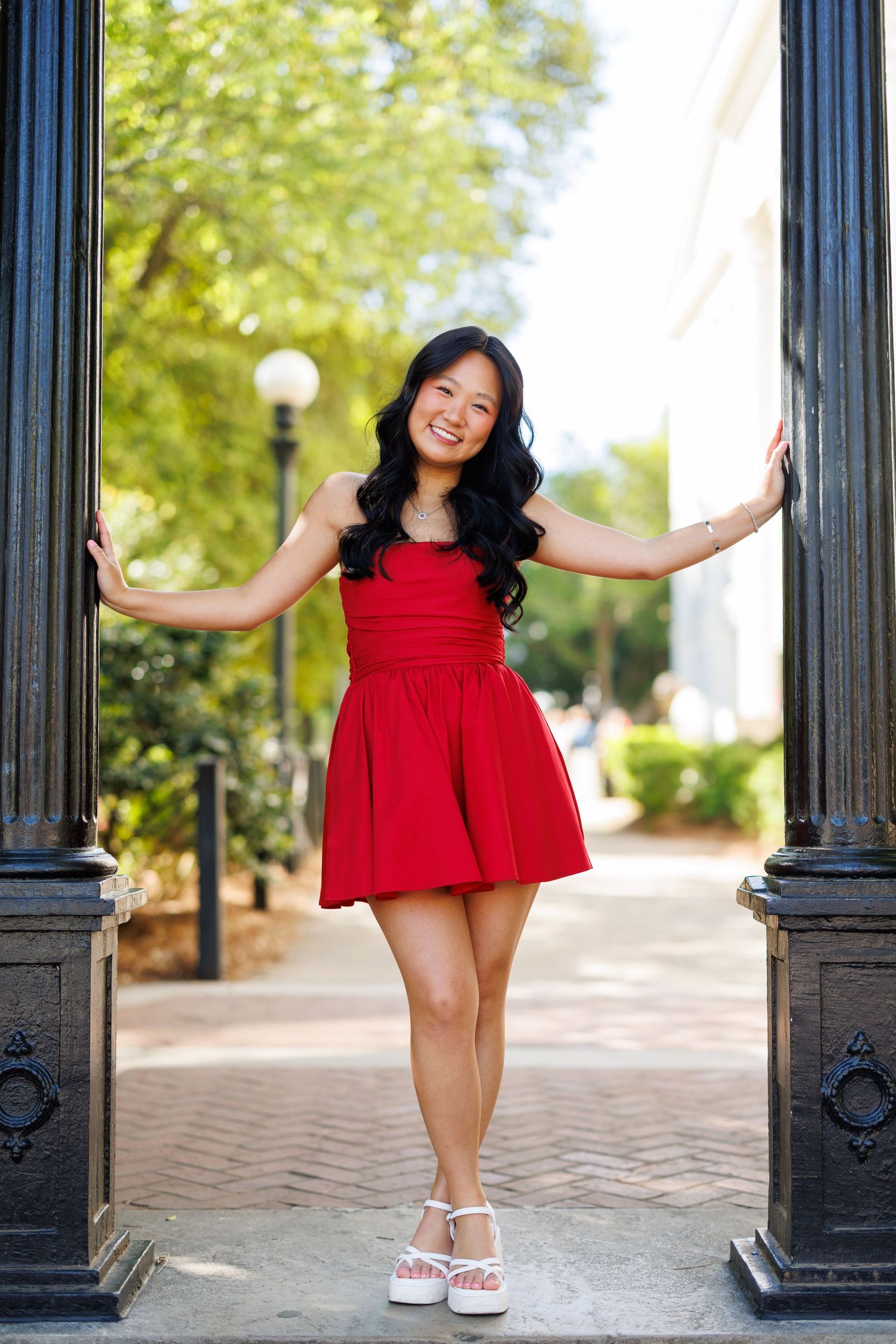 Red dress fashion photos taken along a walkway with decorative black columns.