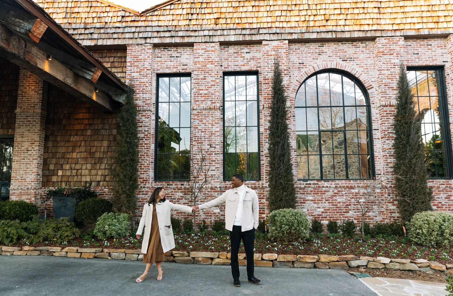Wide panoramic view of a rustic brick building with large windows and wooden roof.