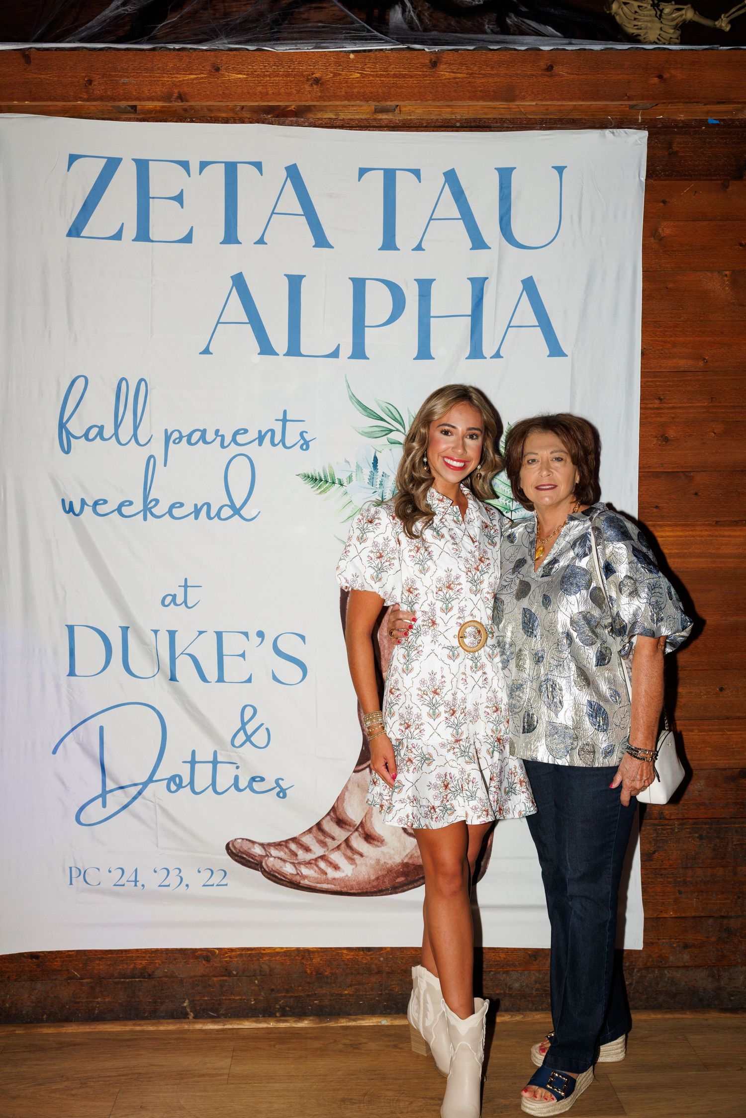 Two women pose at Zeta Tau Alpha fall parents weekend event at Duke's and Dotties sorority banner.