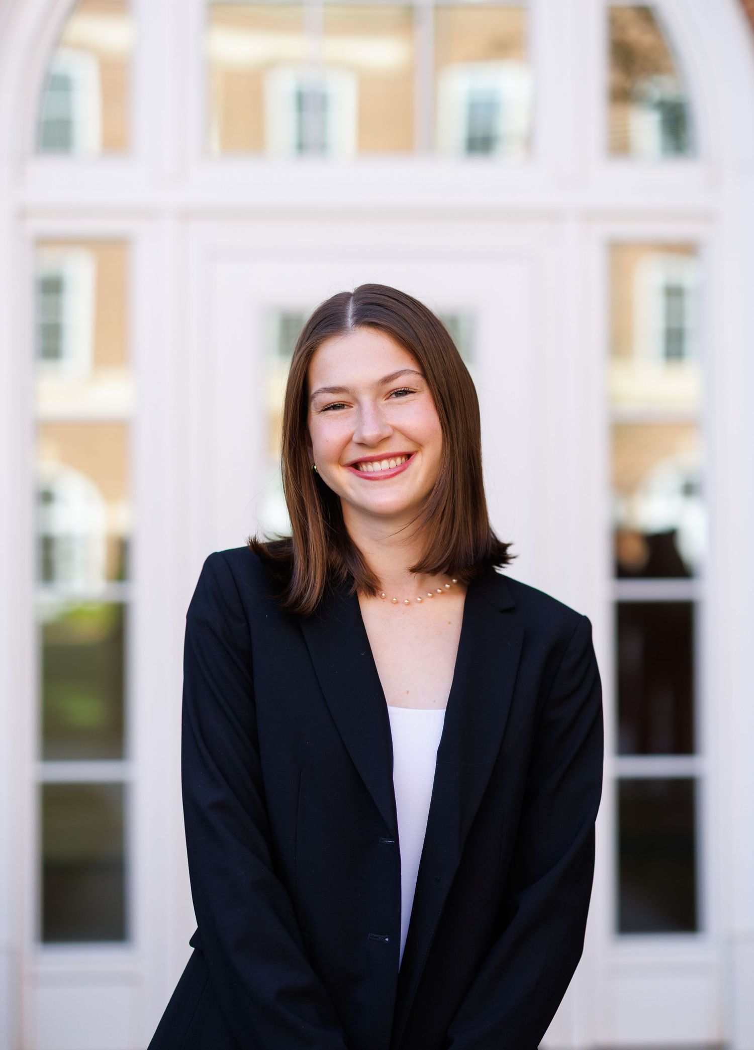 Young woman in black blazer smiling in front of white door at a university building.