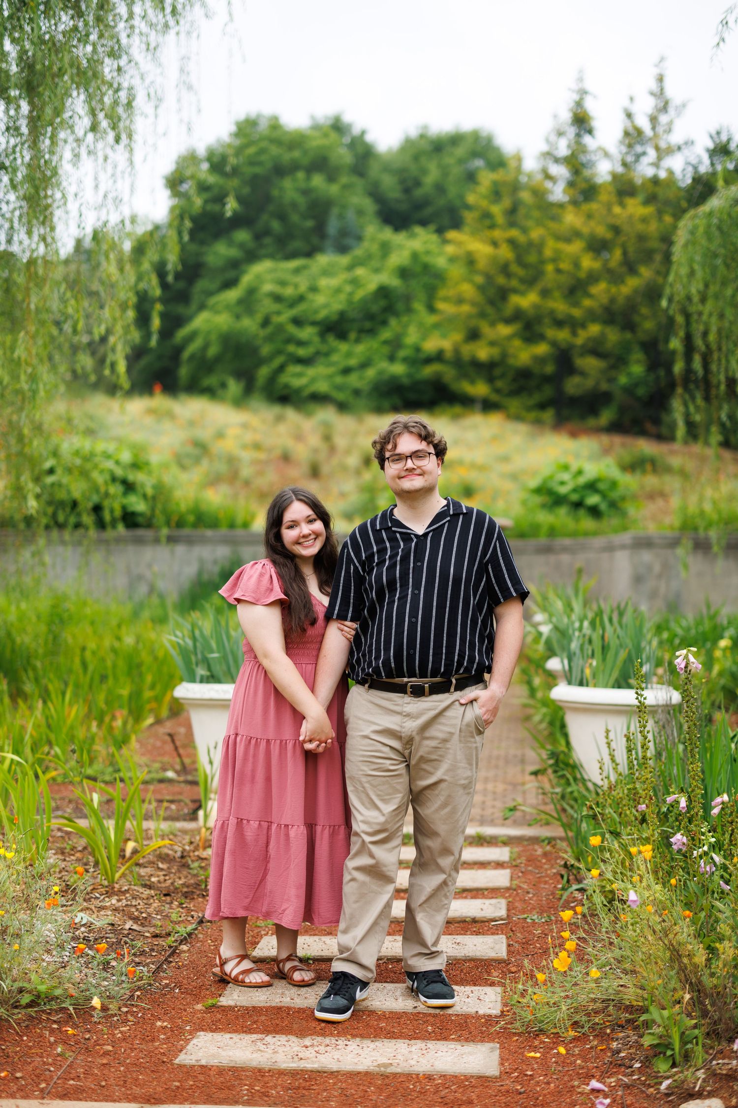 Couple sitting on wooden bench in lush garden setting with willow trees.