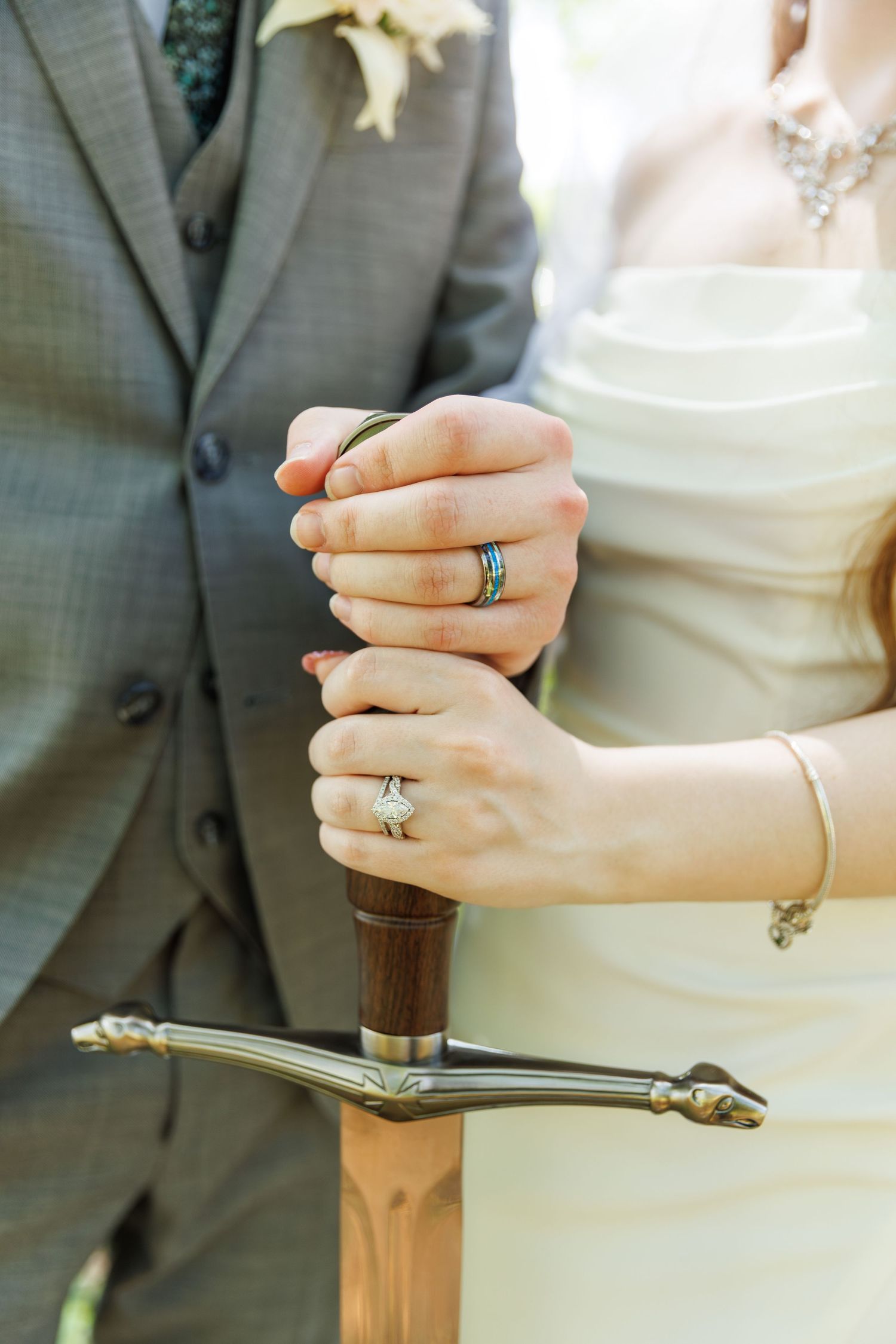 Detail shot of hands holding a ceremonial sword showing wedding rings and formal attire.