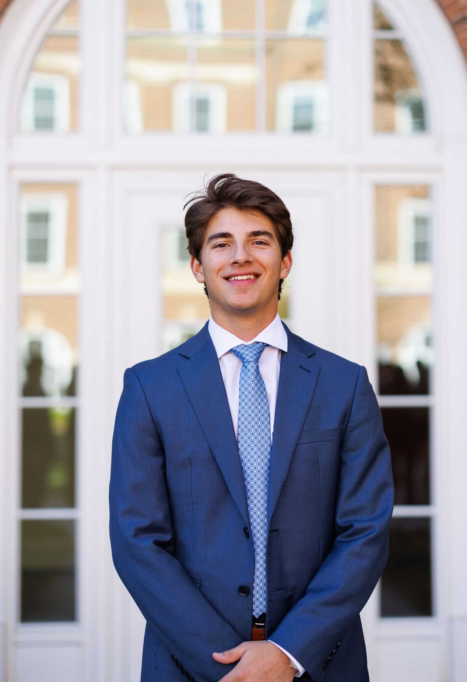 Young man in blue suit and tie smiling in front of elegant arched doorway.
