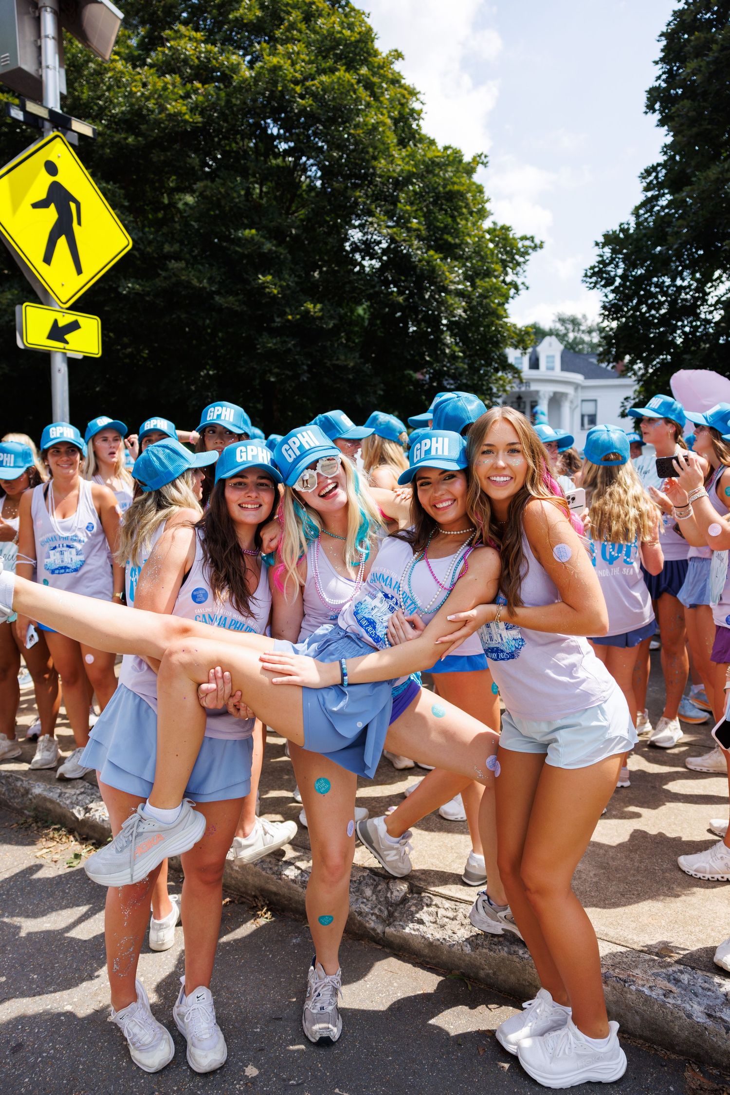 Group of young women in matching blue caps and light blue outfits posing together outdoors at a sunny event.