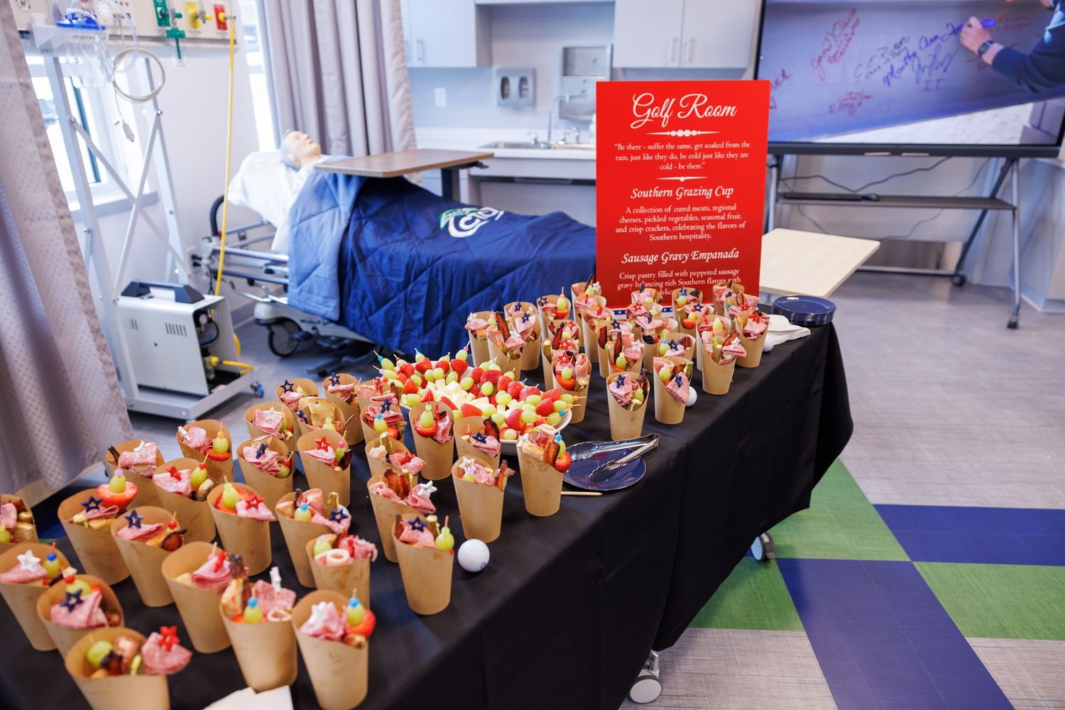 Golf-themed event table with fruit cone appetizers displayed on black tablecloth with red sign in medical facility.