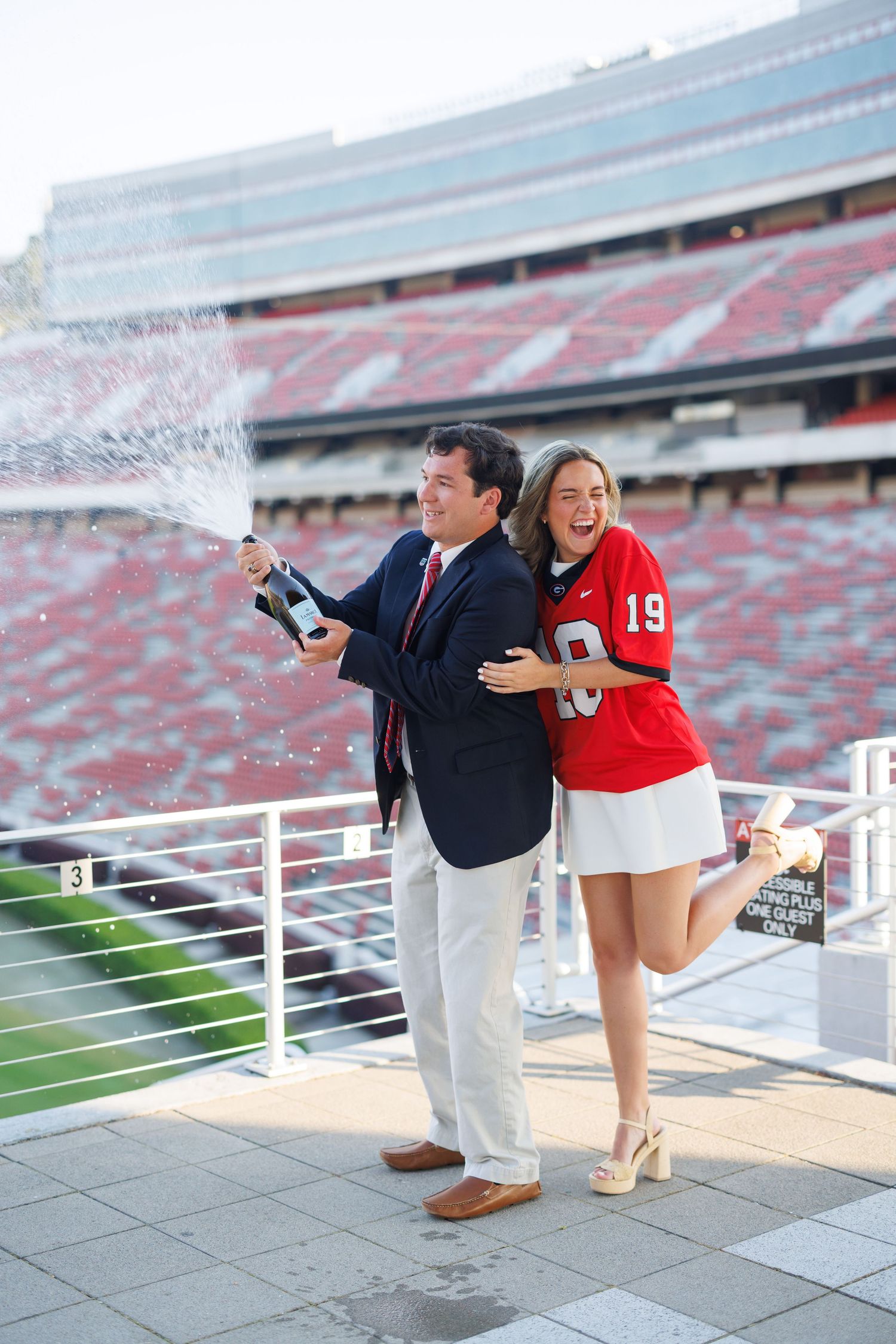 A couple in Ohio State colors pose playfully at the edge of Ohio Stadium during an engagement photo session.