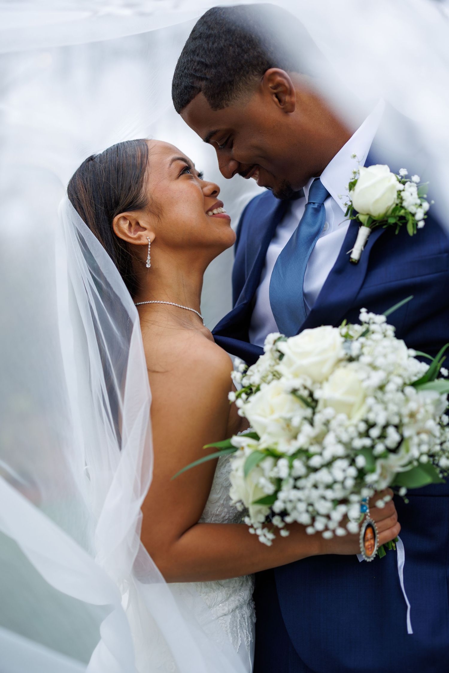 An intimate wedding portrait with a white bouquet and elegant veil against a light background.