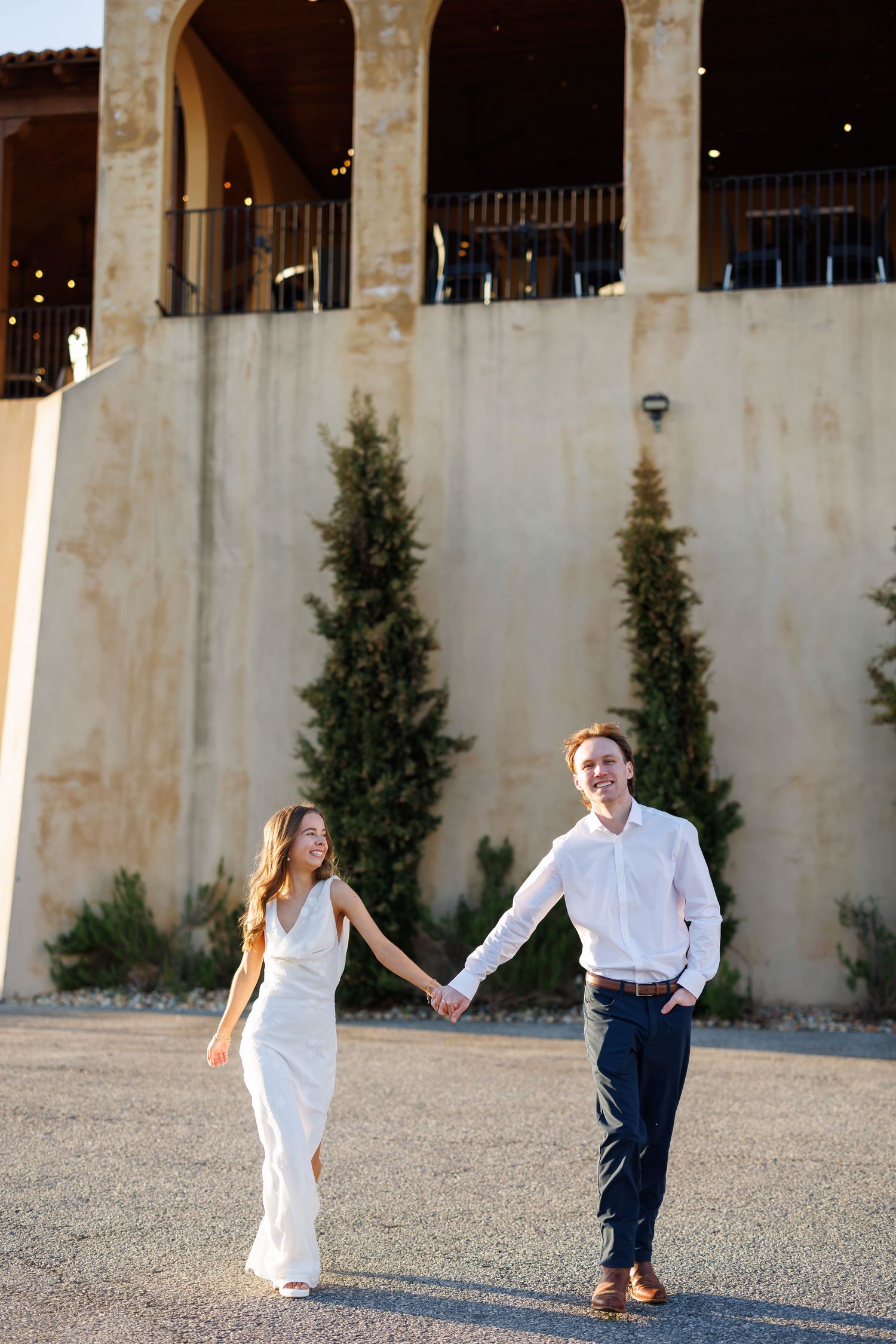 Playful couple dancing and twirling on stone patio with arched architecture.