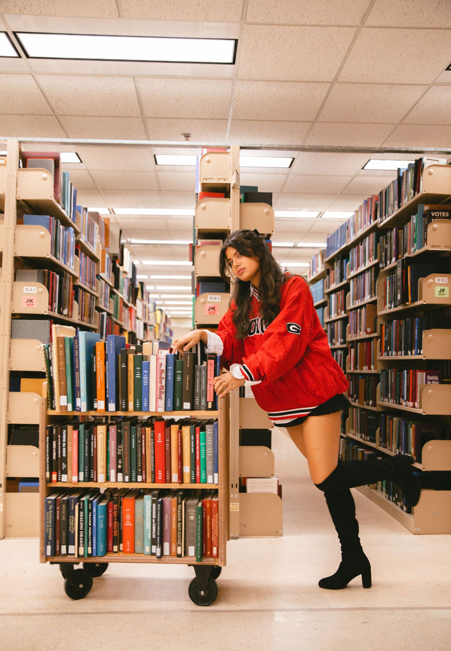 Playful photo series of someone posing between library bookshelves wearing red and black.