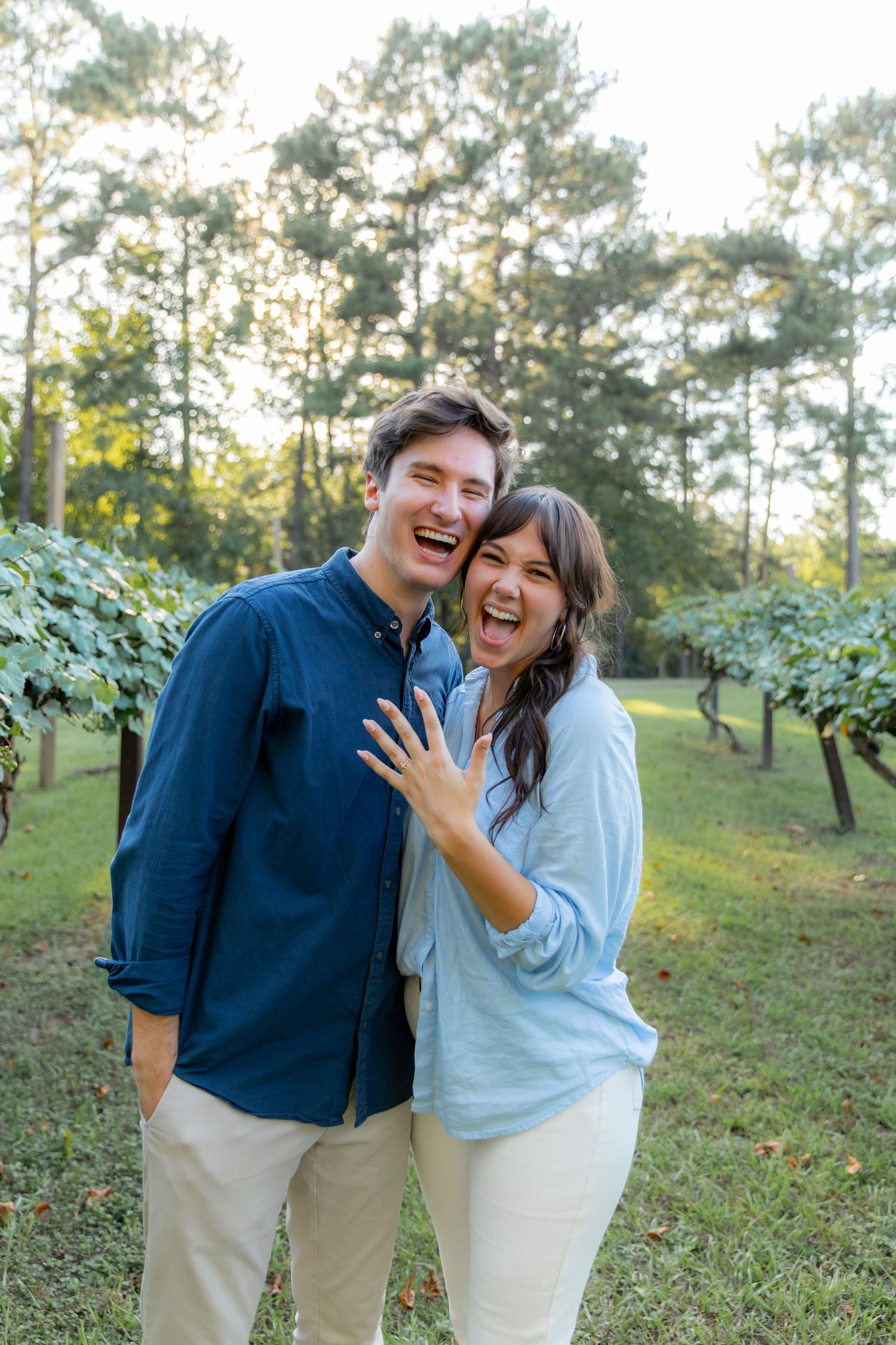 Joyful couple laughing and embracing in sunny vineyard setting.