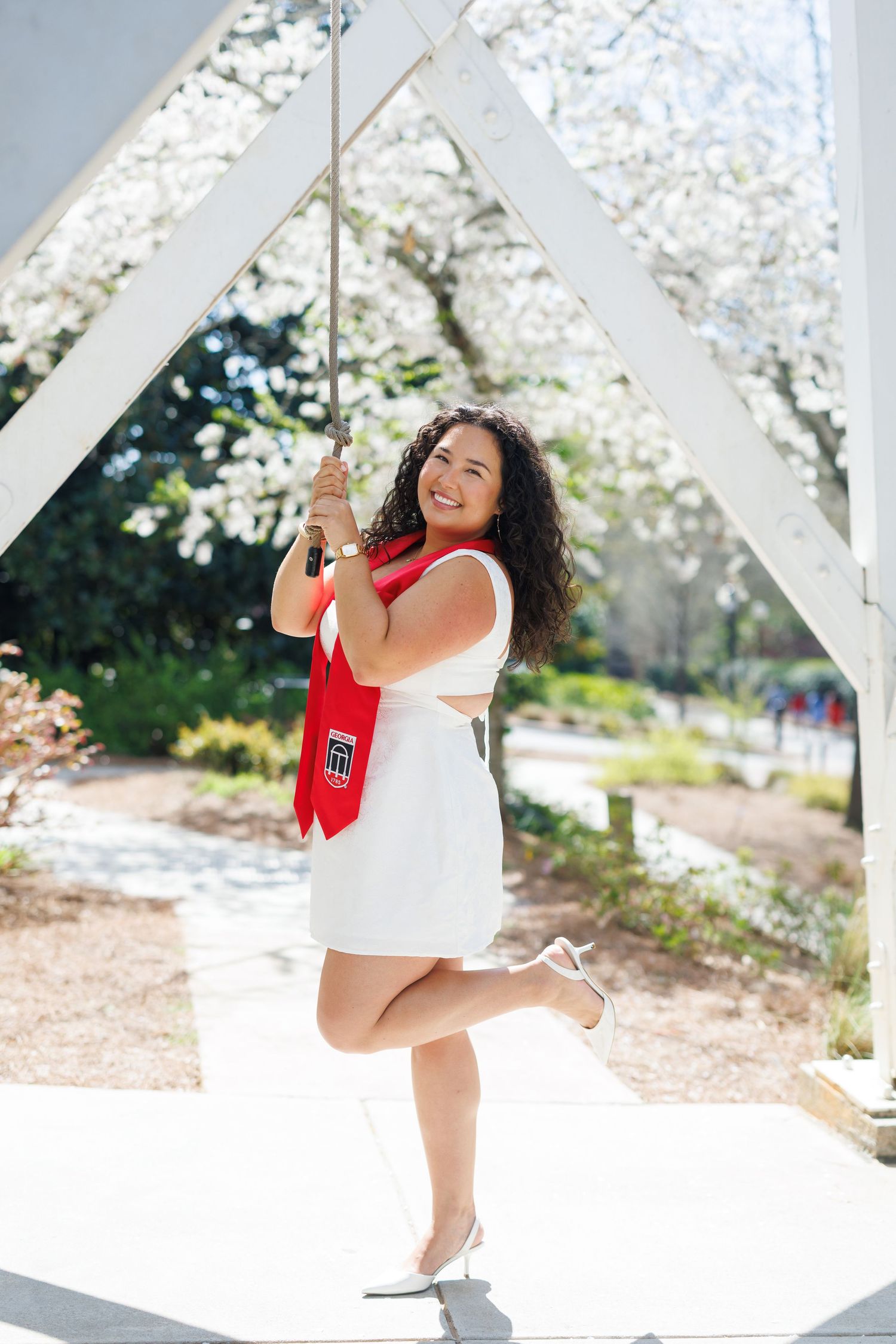 A person in a white top and shorts enjoys swinging outdoors on a sunny day with cherry blossoms in bloom.