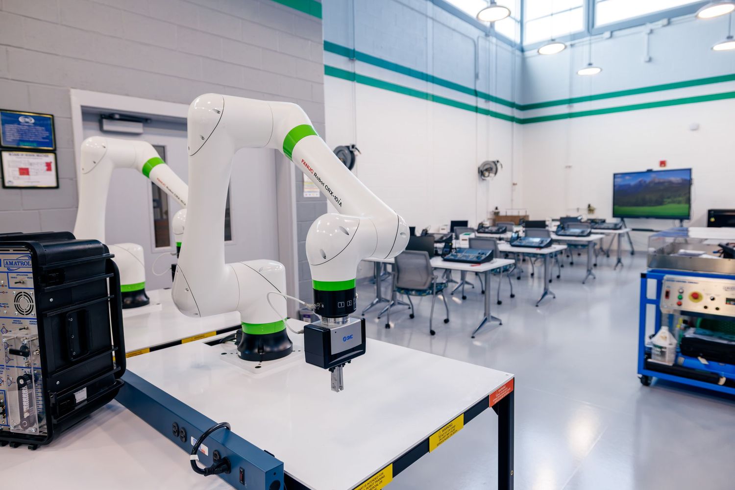 White and green robotic arm in a modern industrial lab classroom with workstations and equipment.