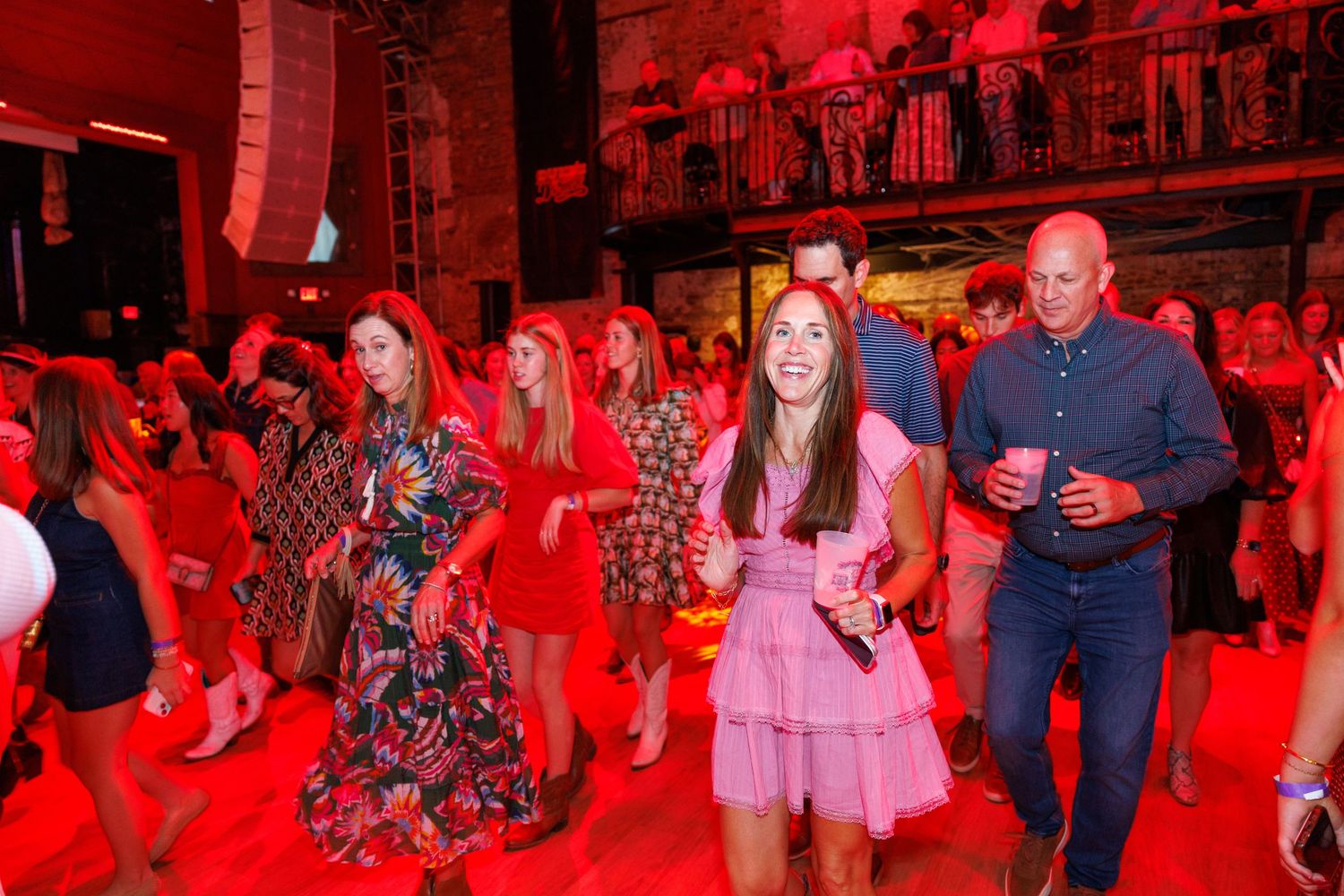 Guests dancing and socializing at a vibrant red-lit indoor party event wearing colorful dresses.