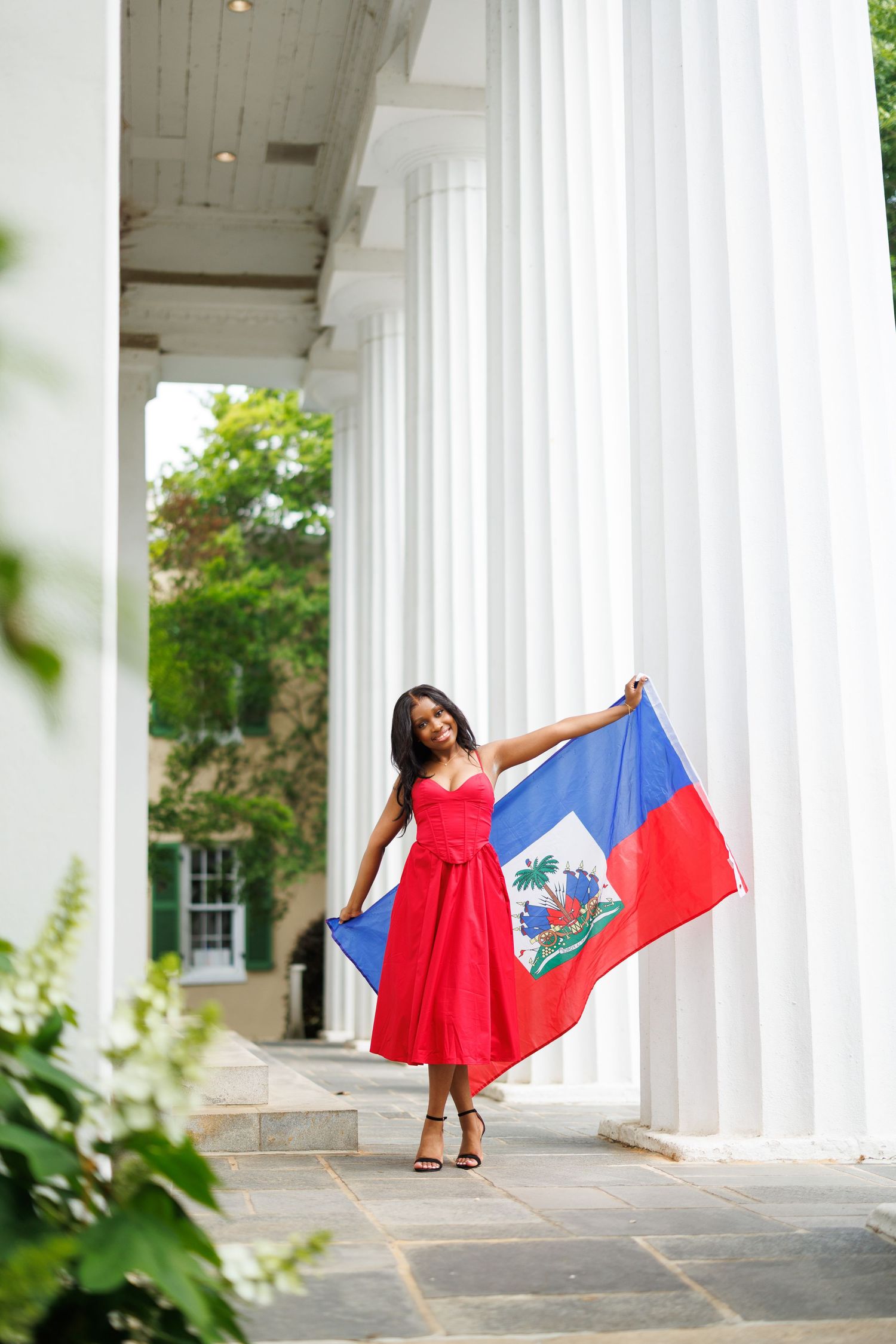 Dancing with the Haitian flag among white columns in a red dress.