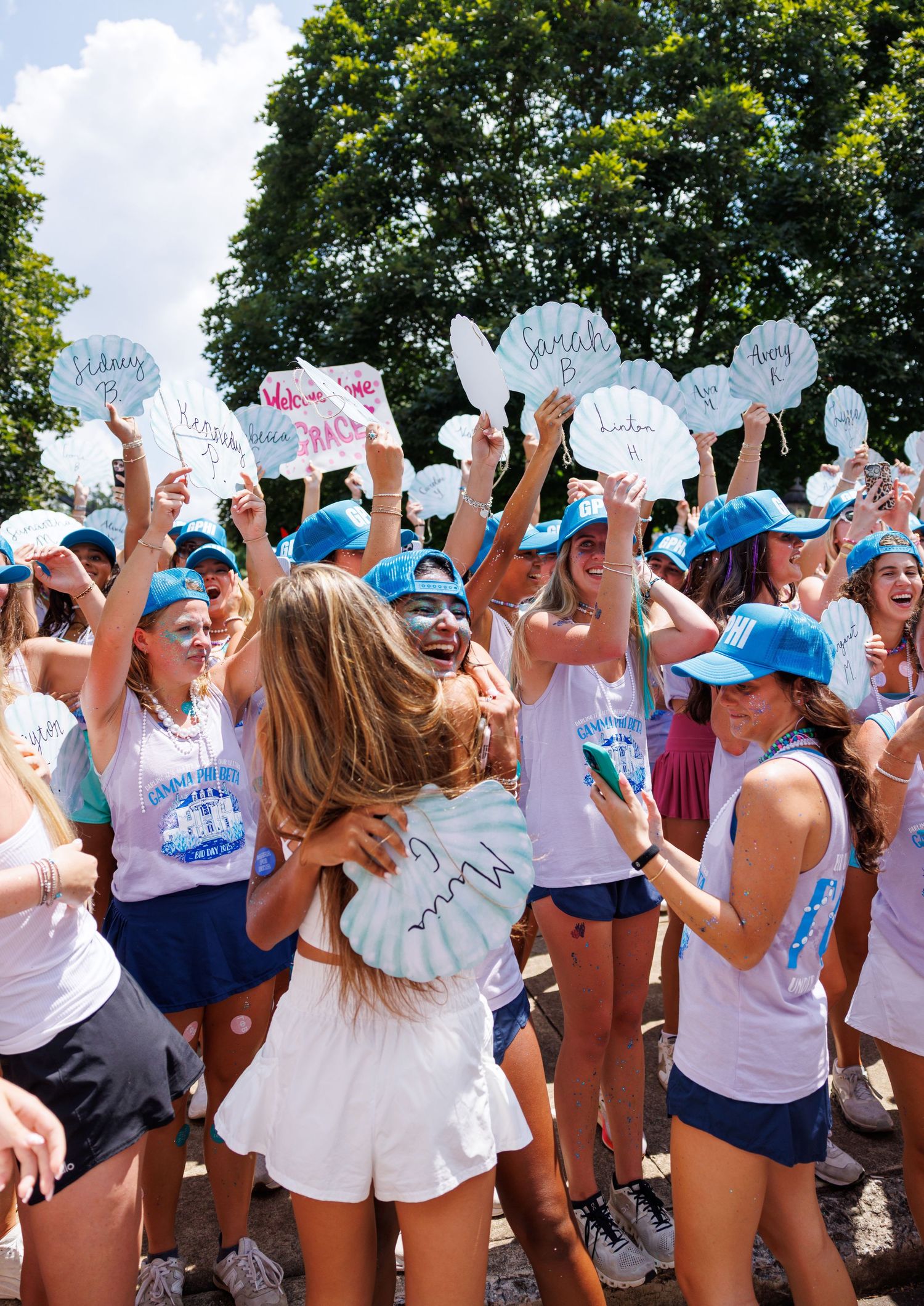 Sorority members holding name signs embrace new recruits during a joyful bid day celebration outdoors.