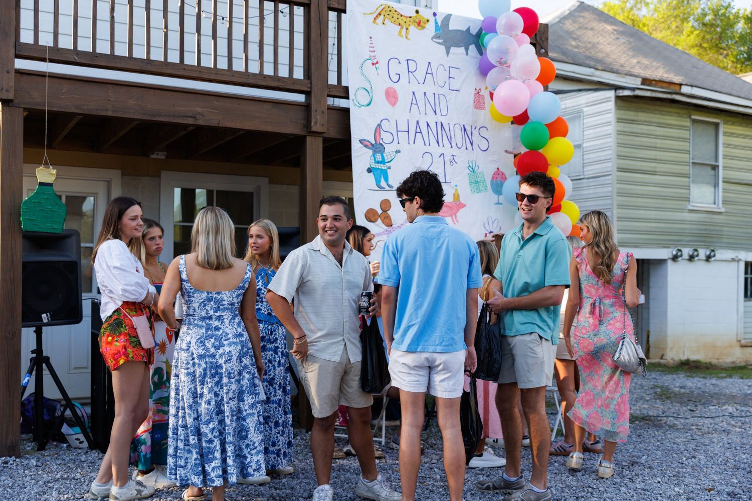Group of friends gathered outdoors at Grace and Channing's celebration party with colorful balloons and festive banner.