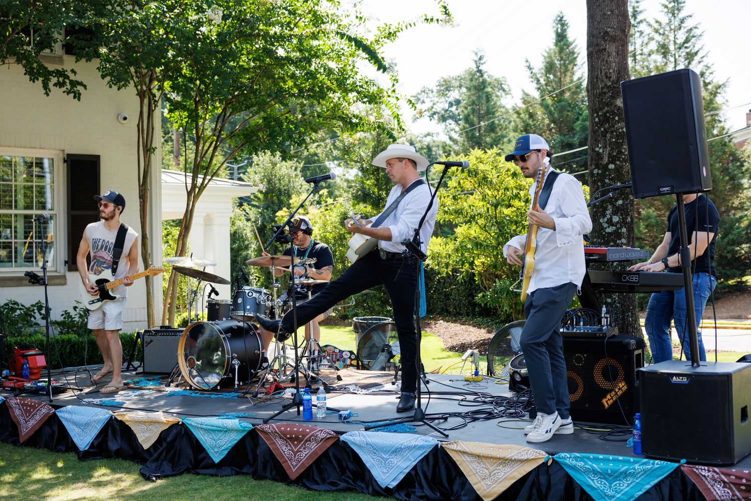 Live band performing outdoors on a decorated stage at a garden party on a sunny day.