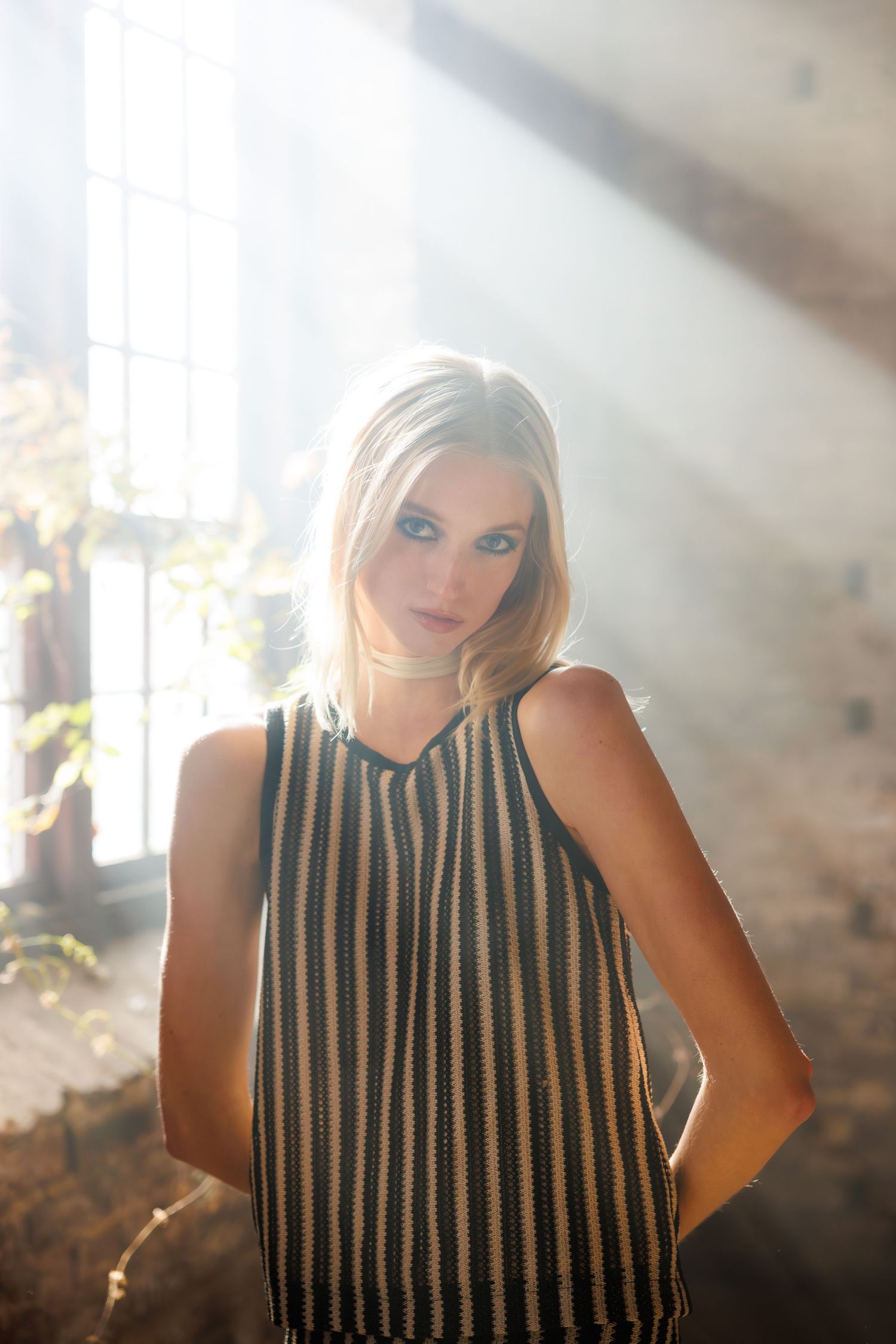 Fashion portrait of woman in striped top with dramatic sunlit backdrop.
