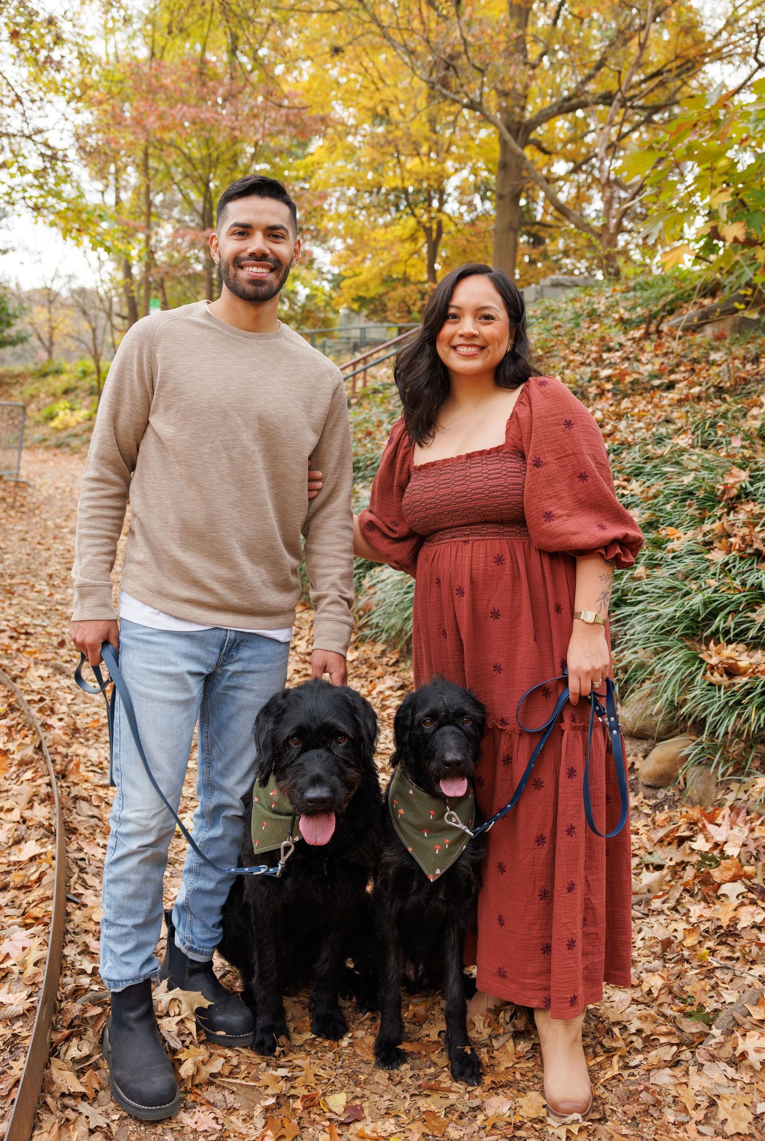 Fall family portrait with two black dogs among autumn leaves.