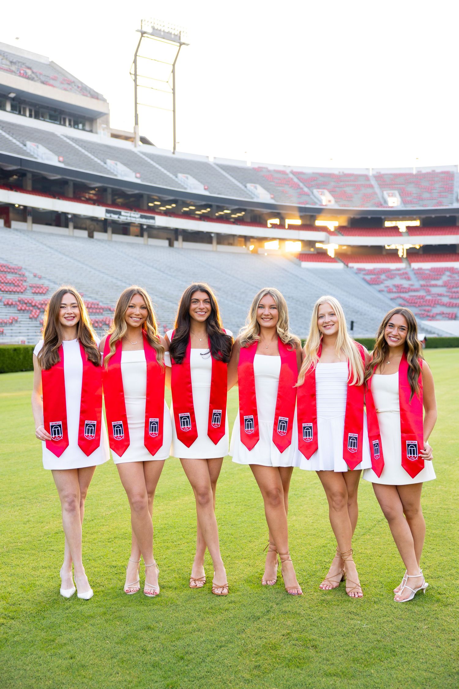Group wearing red graduation stoles pose together on football field at University of Georgia stadium.