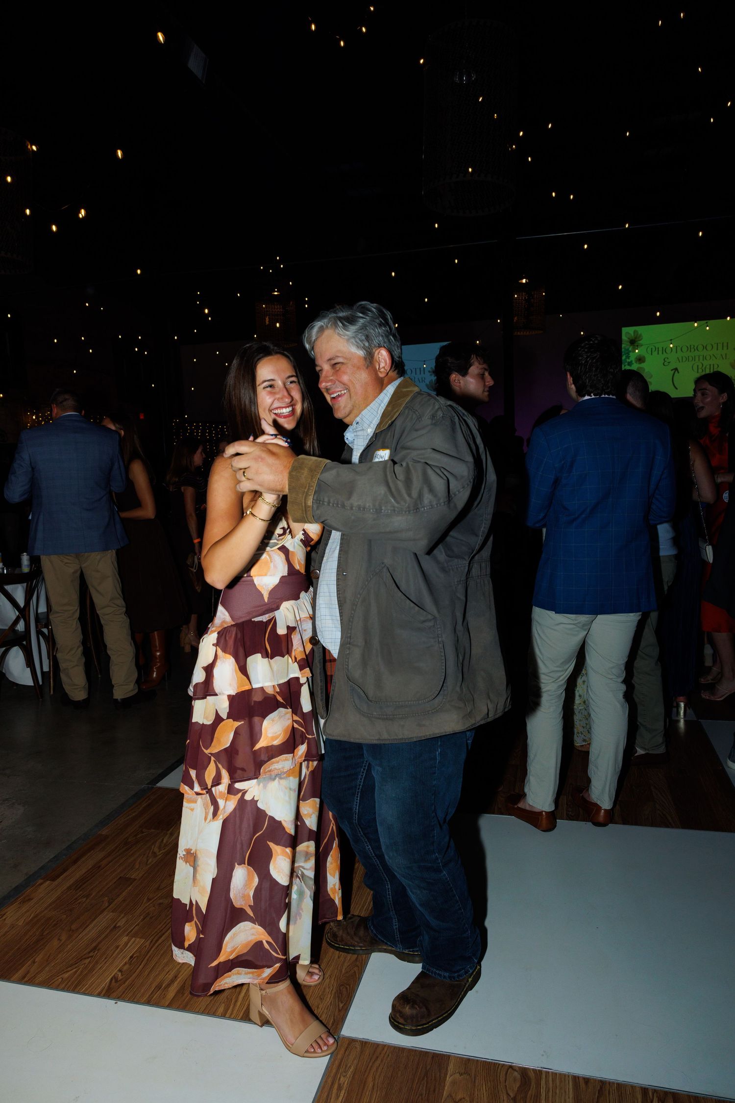A man and woman dancing together at an evening event, smiling joyfully on a dance floor with guests in the background.