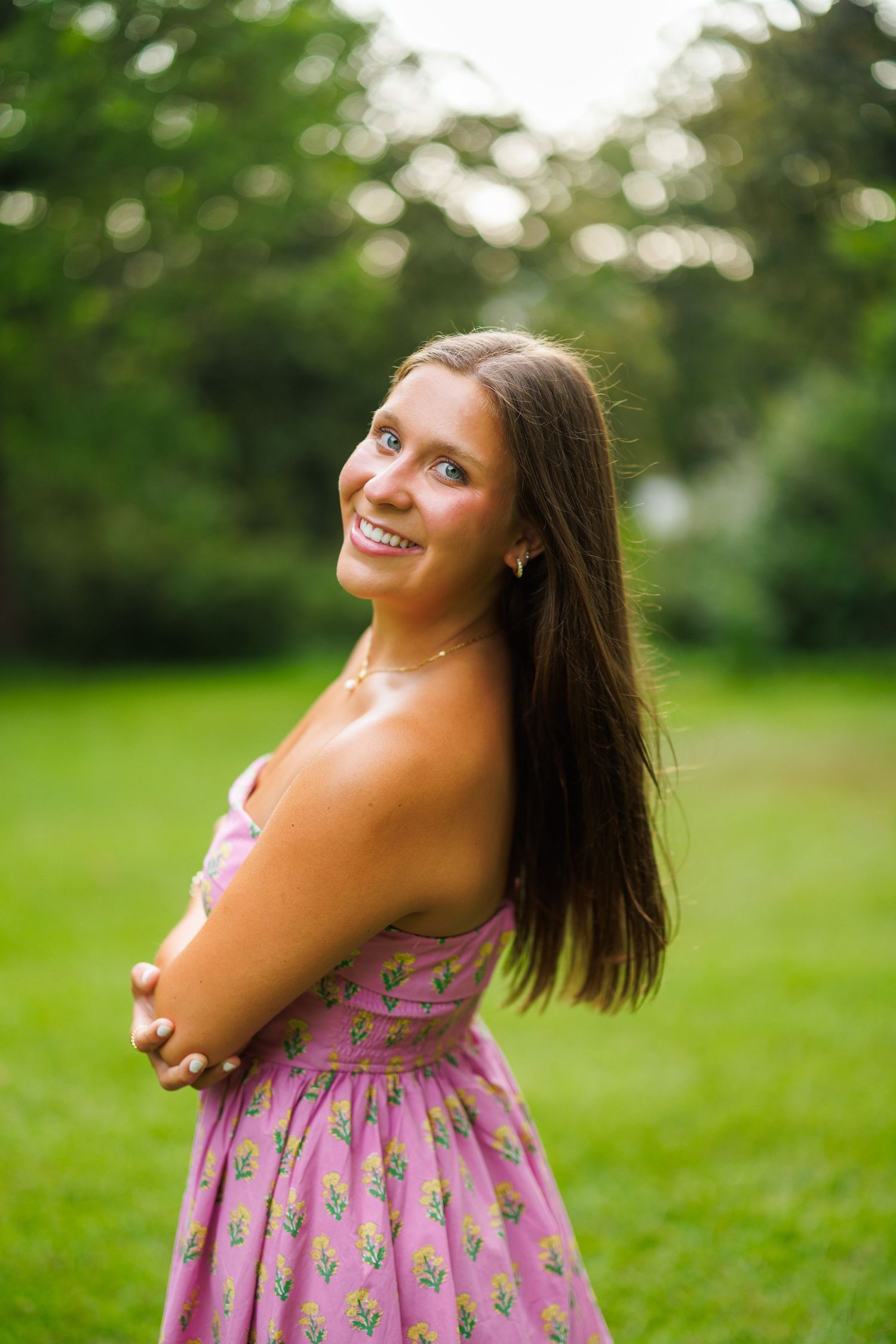 A person in a pink floral dress poses playfully in a green outdoor setting during a photo session.