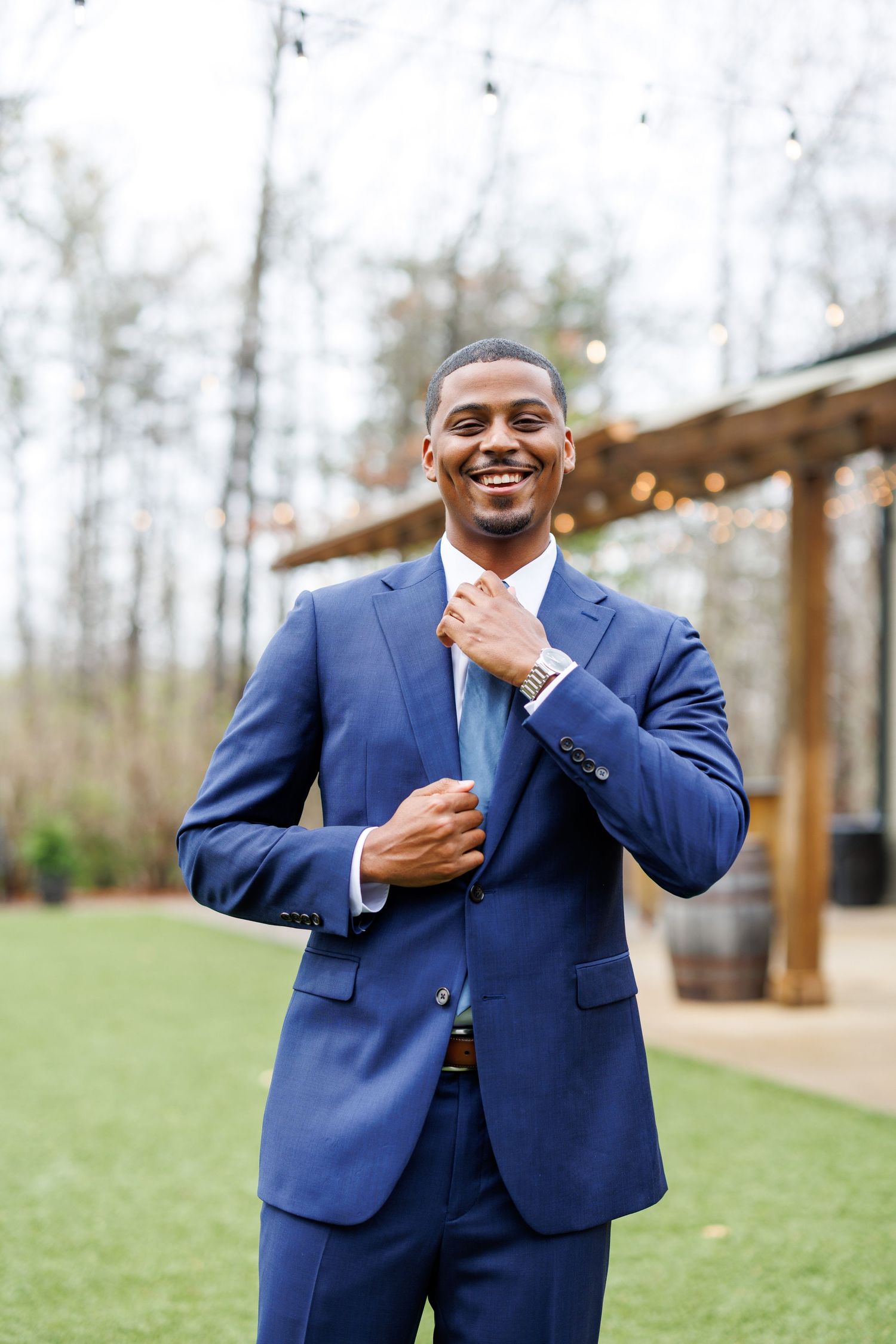 A person in a navy blue suit adjusts their tie while standing outdoors.