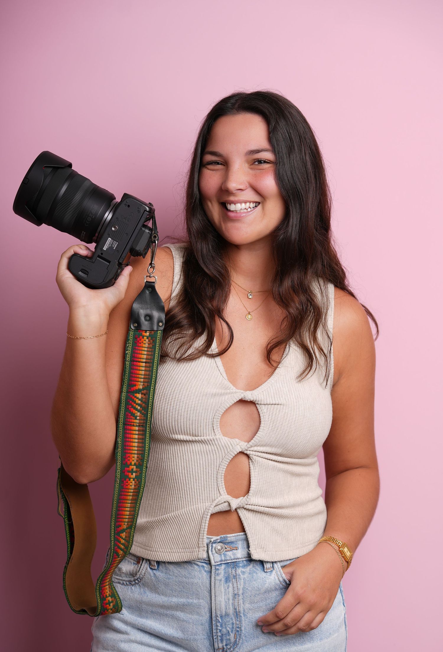 Photographer poses with professional camera against pink backdrop in studio setting.