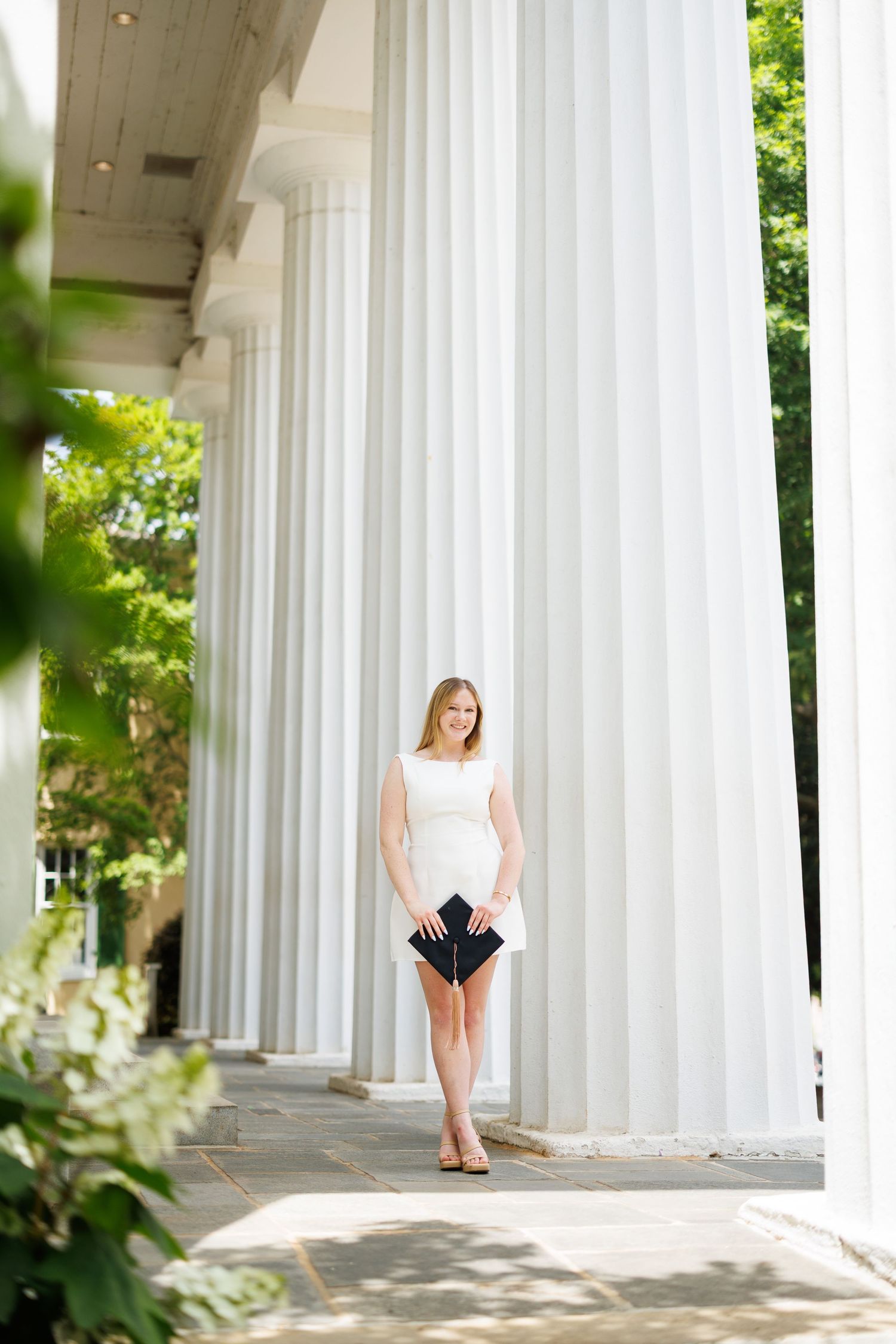 A ballet dancer performs graceful poses between white classical columns in an outdoor setting.