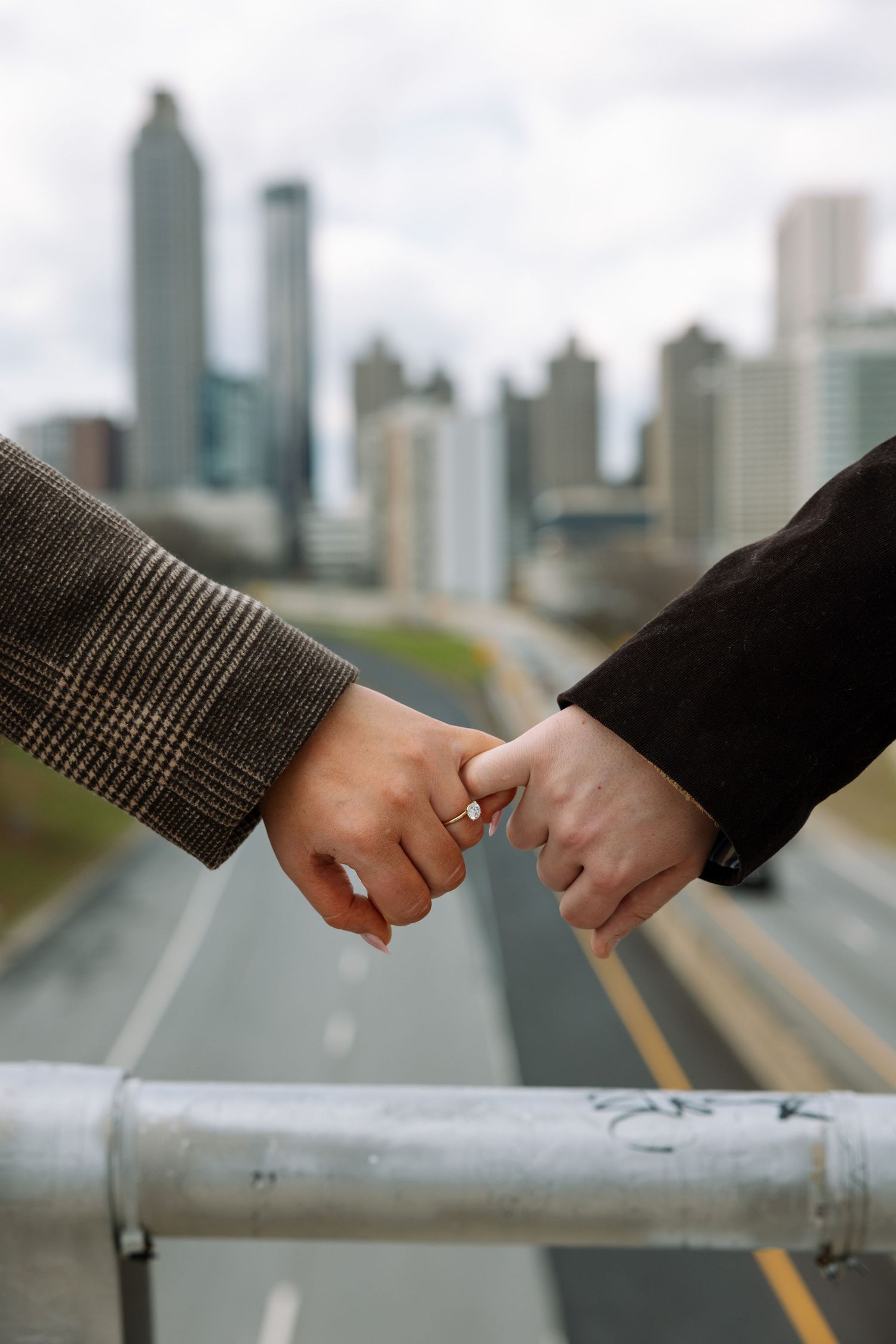 Close-up of two hands touching on a railing with a city skyline in the background.
