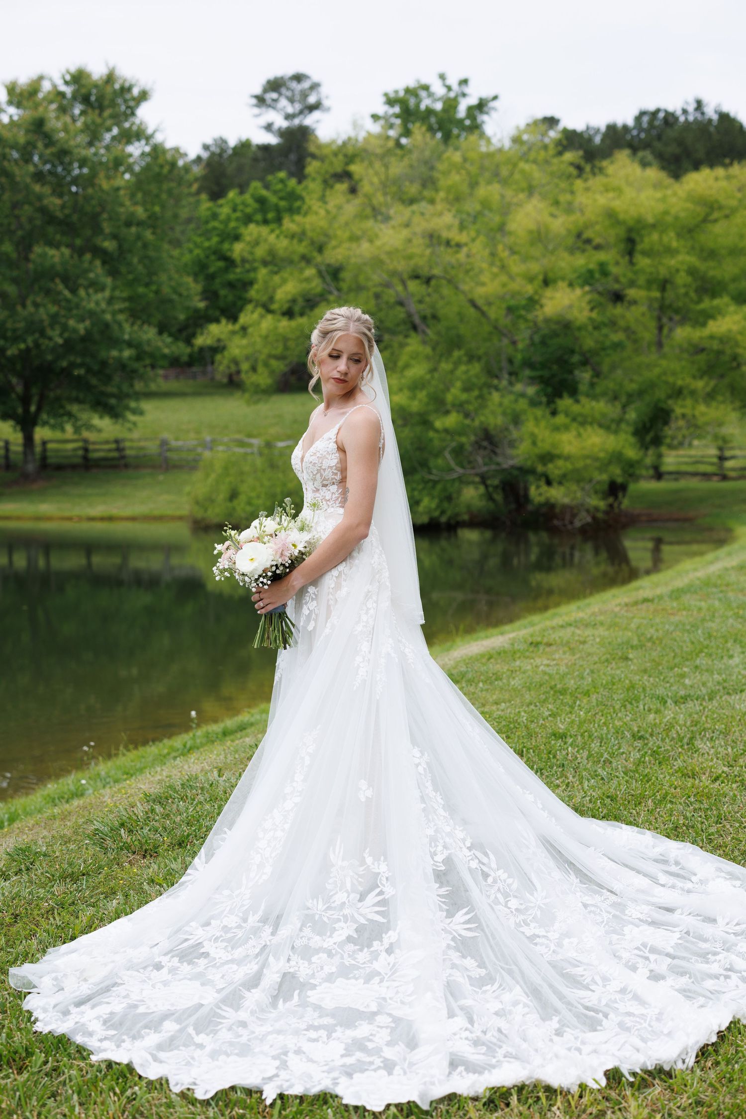 Dramatic full-length shots of a wedding dress with cathedral train spread out on green grass.