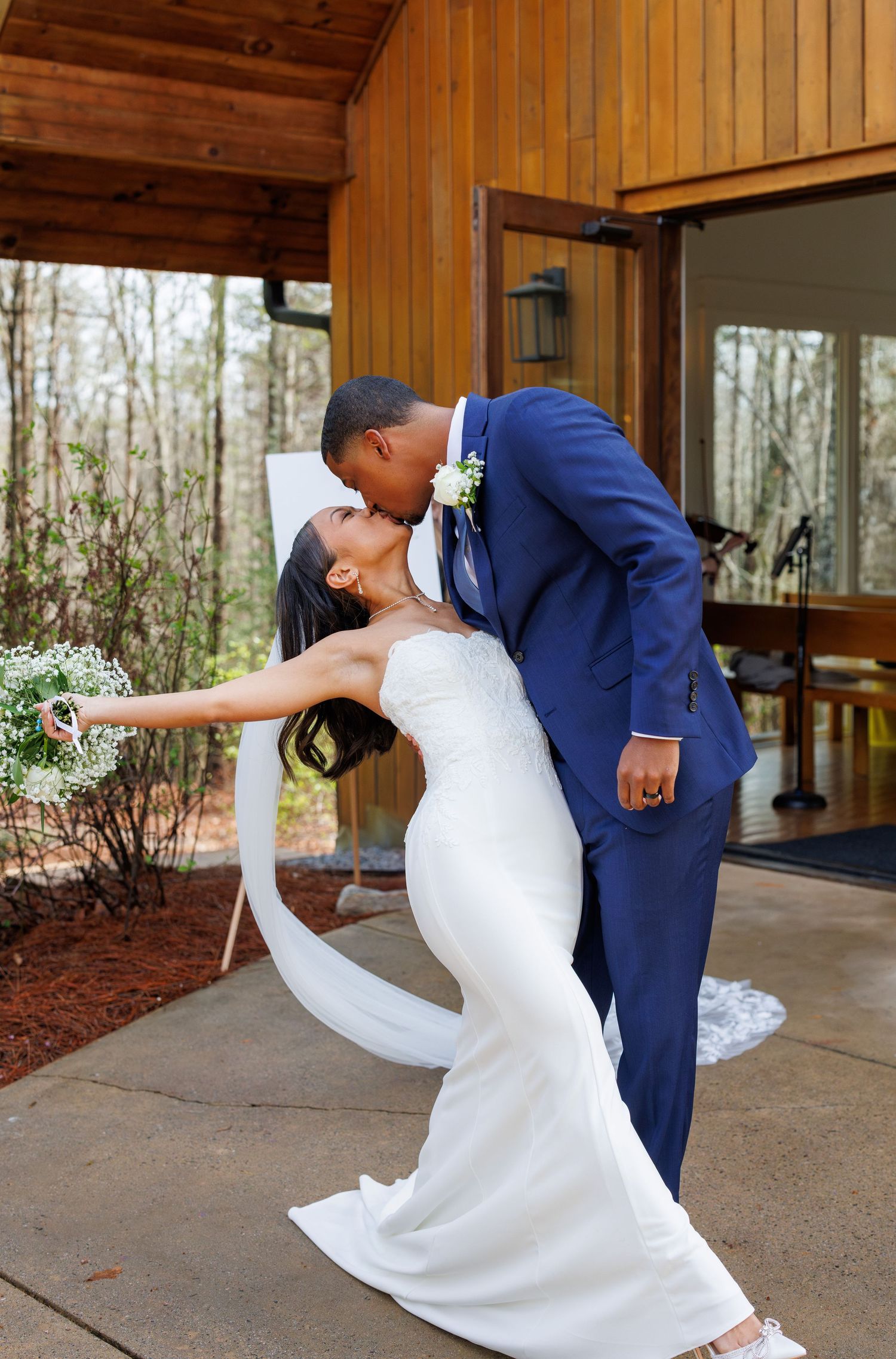 A romantic outdoor wedding dip pose with a flowing white dress and navy suit.