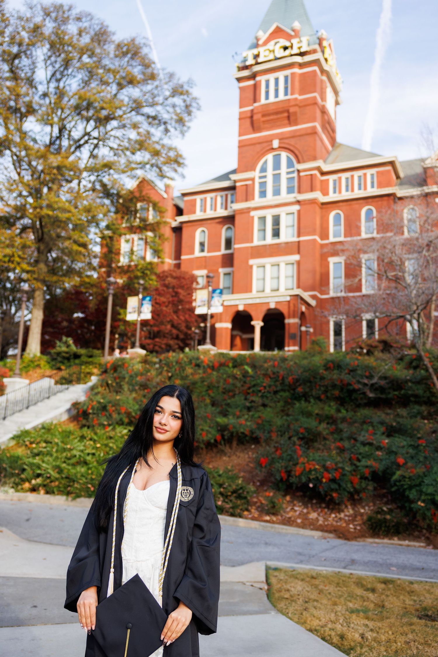Graduate poses in front of historic red brick university building during fall season.