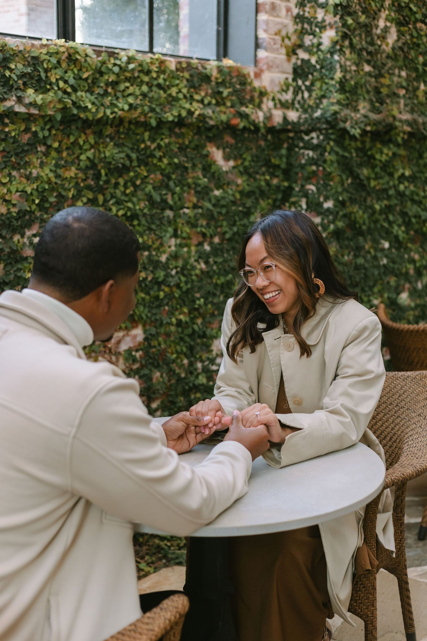 A couple shares an intimate moment at an outdoor table with ivy-covered walls in the background.