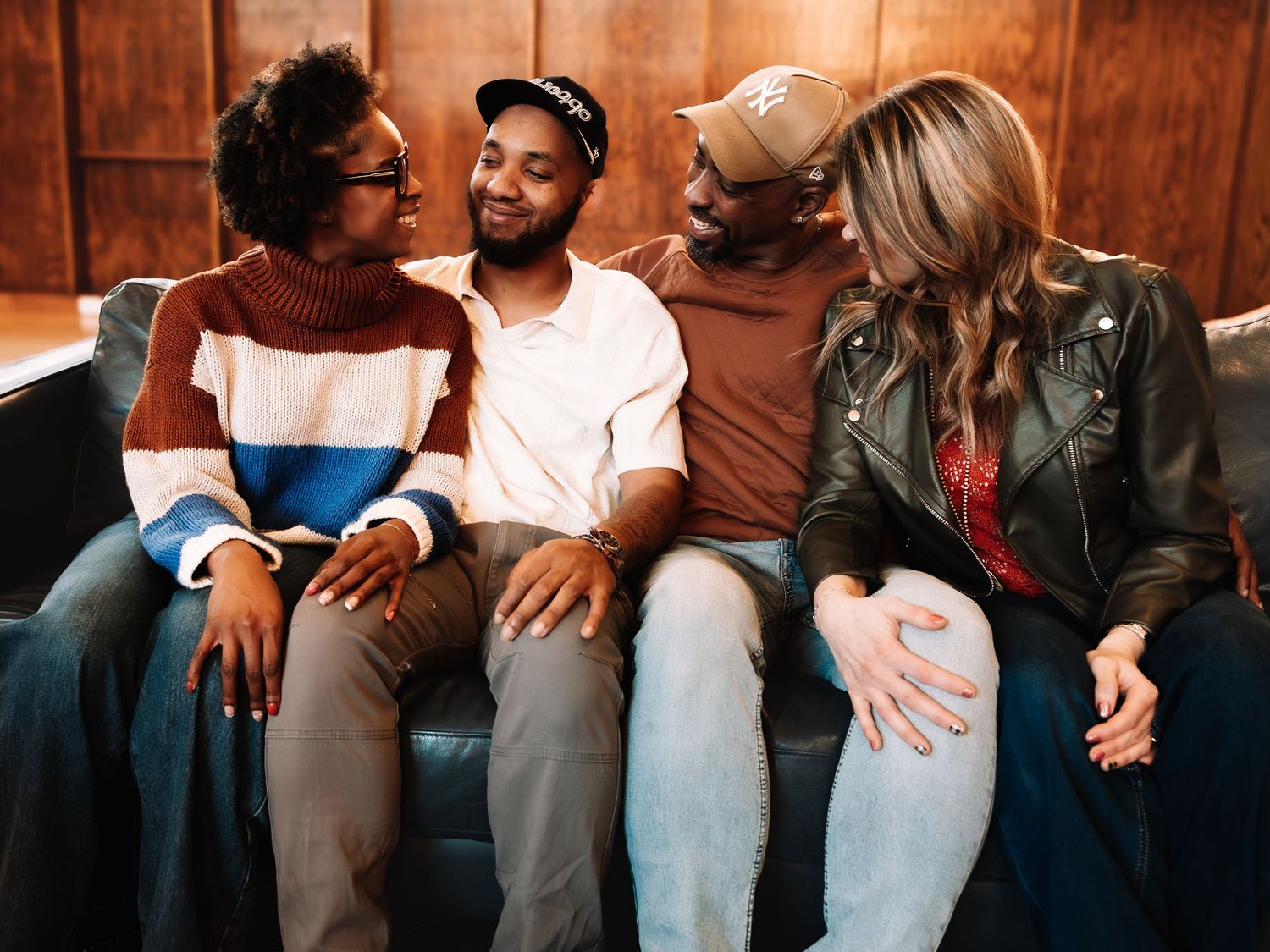 Four friends laughing and bonding together while sitting on a couch in a warmly lit room.