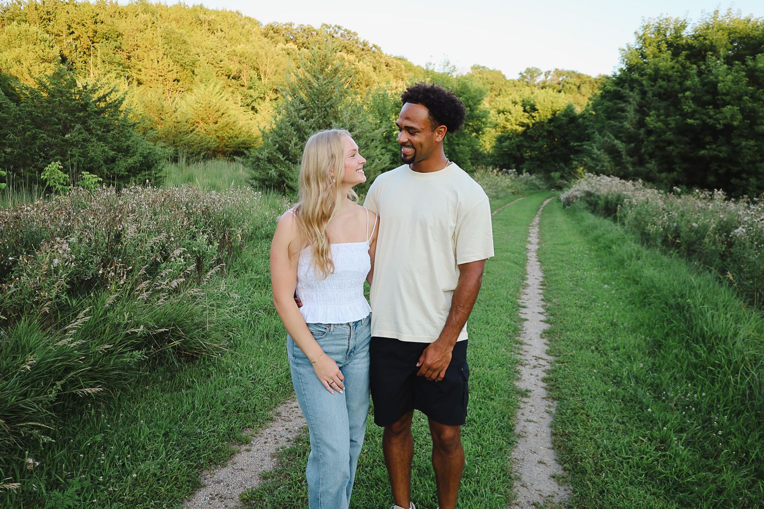Couple walking together on a scenic grassy path during golden hour.