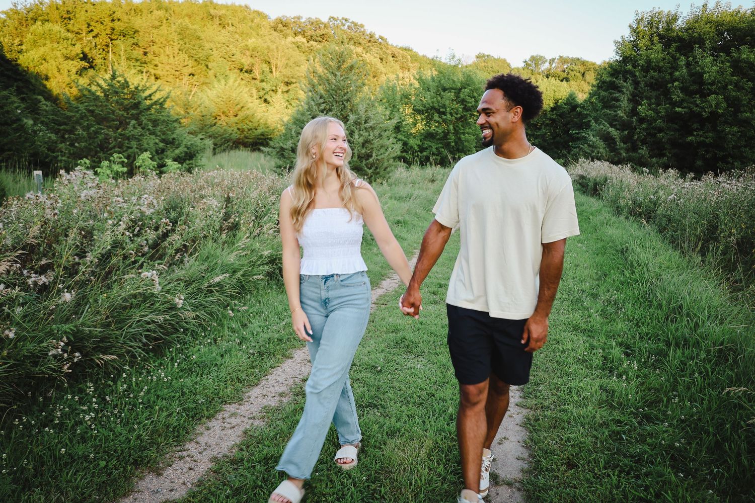 A couple walking and laughing together on a scenic dirt path in nature.