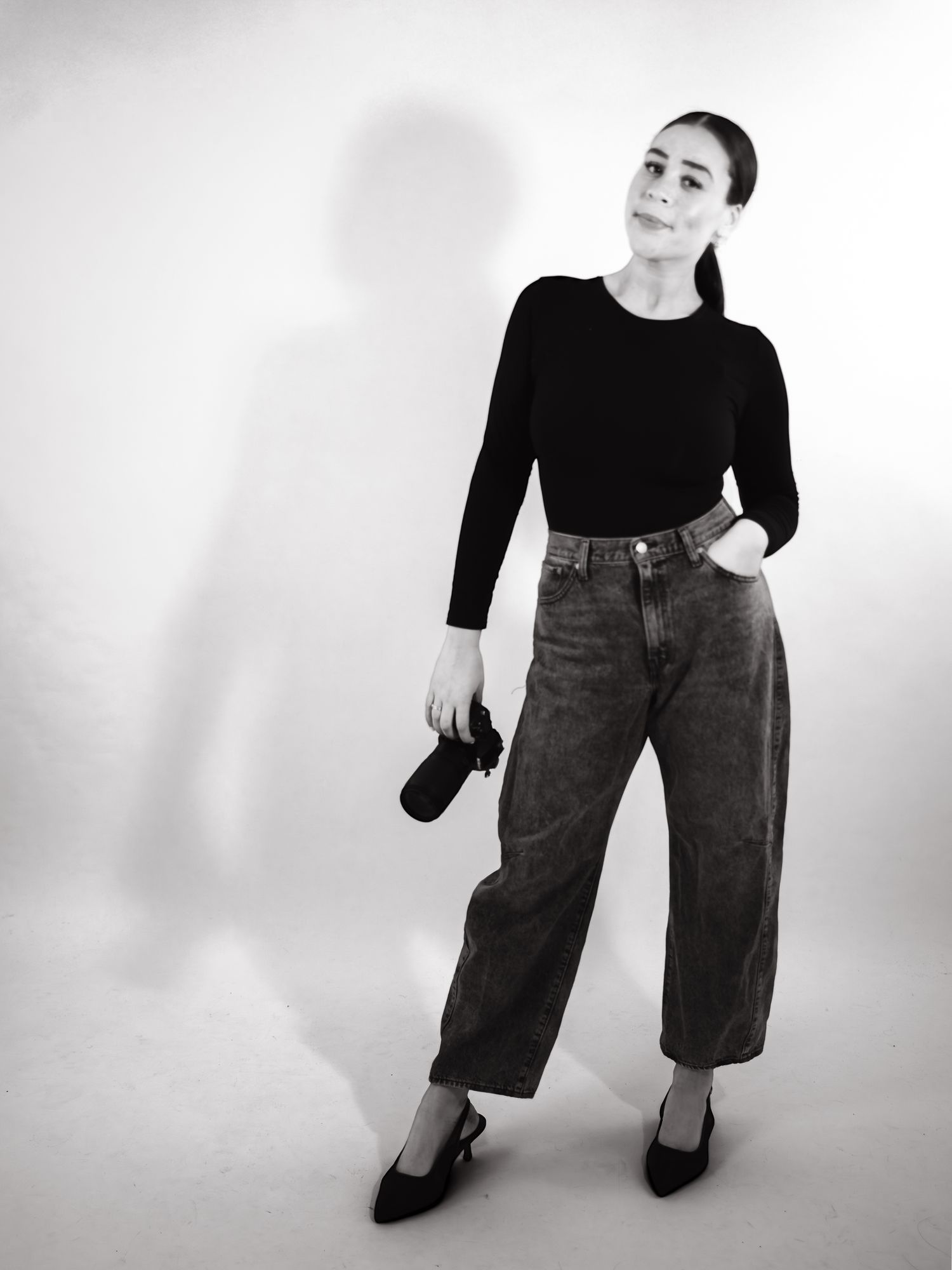 Figure in black top and wide-leg jeans poses dynamically against white backdrop.
