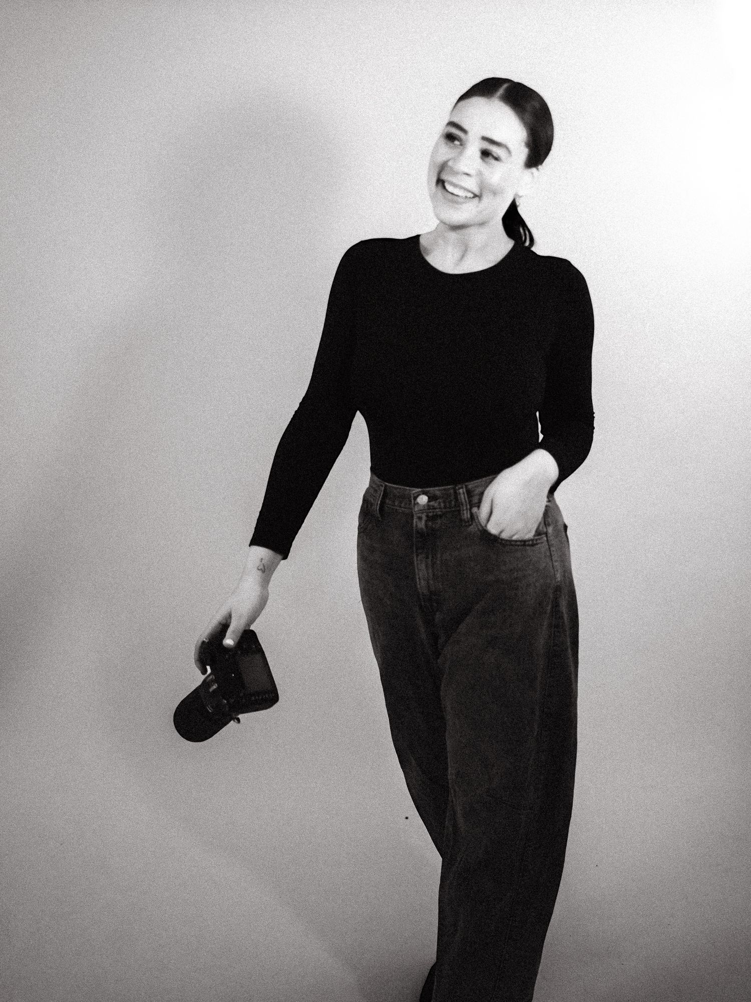 Figure in black clothing performs expressive dance movements in a minimalist studio setting.