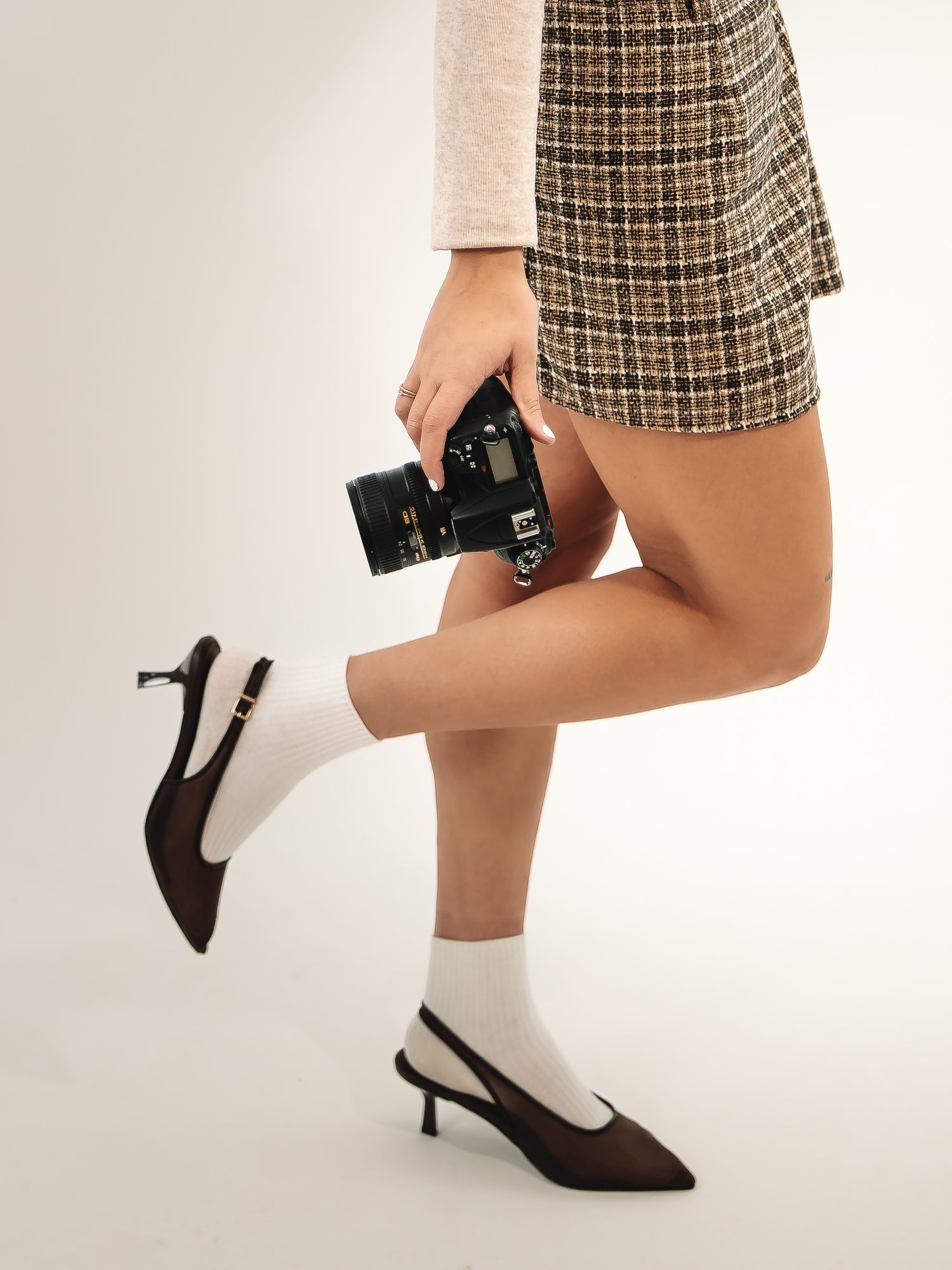 Fashion detail shots of legs in plaid skirt and heels holding camera.