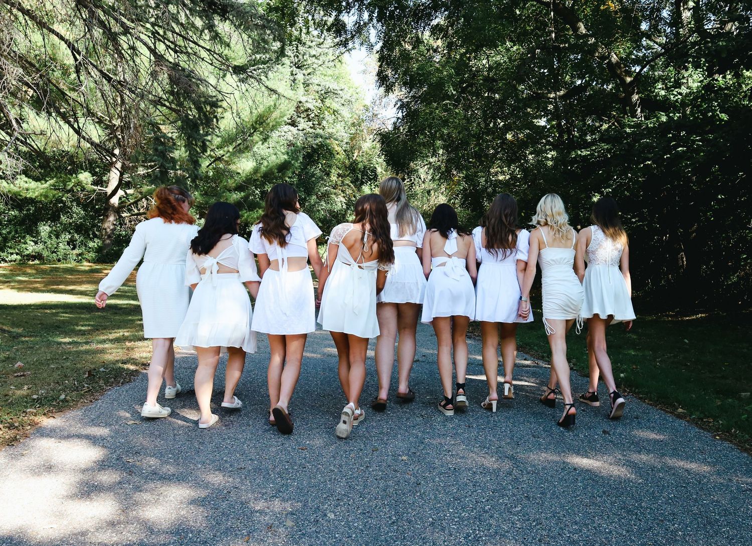 Group wearing matching white dresses walking together on garden pathway.