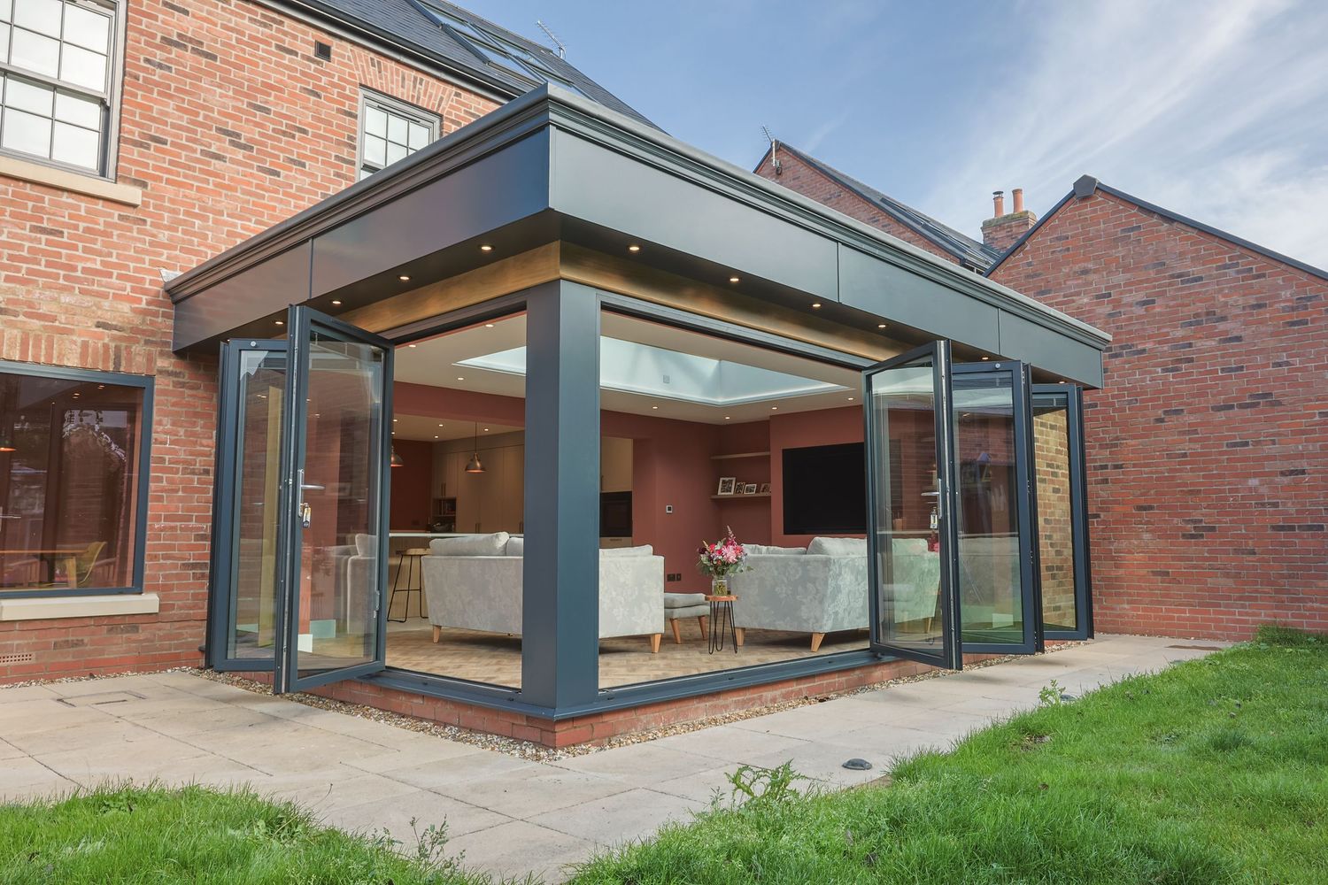Modern glass extension with bifold doors on a traditional brick house with a patio garden.