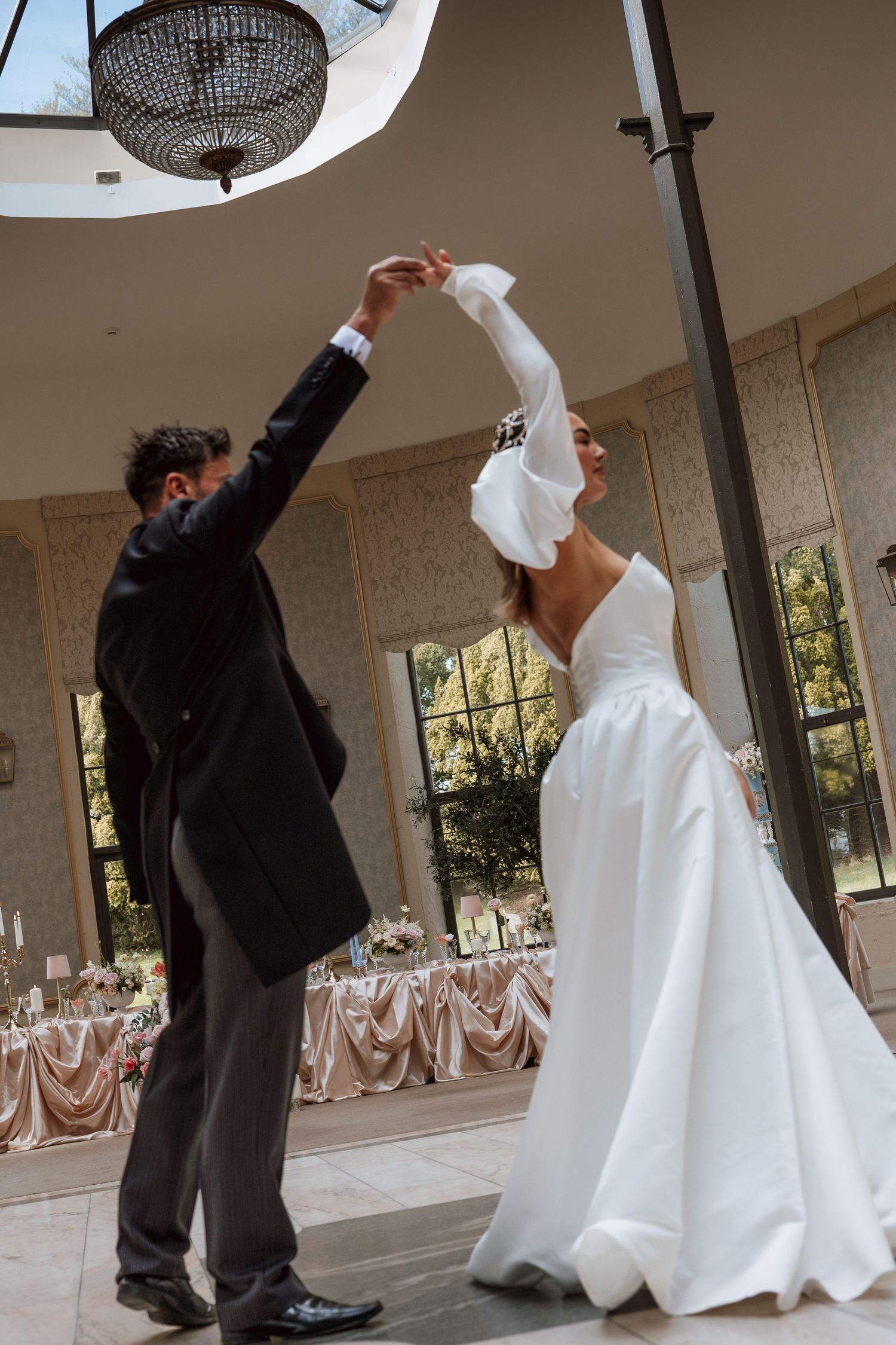 Bride and groom share their first dance in an elegant wedding reception hall with crystal chandelier overhead.