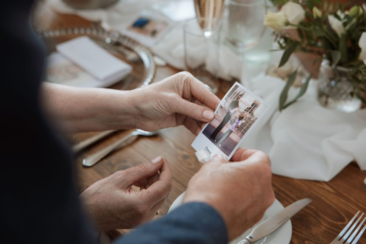 Guest holds a small Polaroid photo of the wedding couple at a decorated reception table.